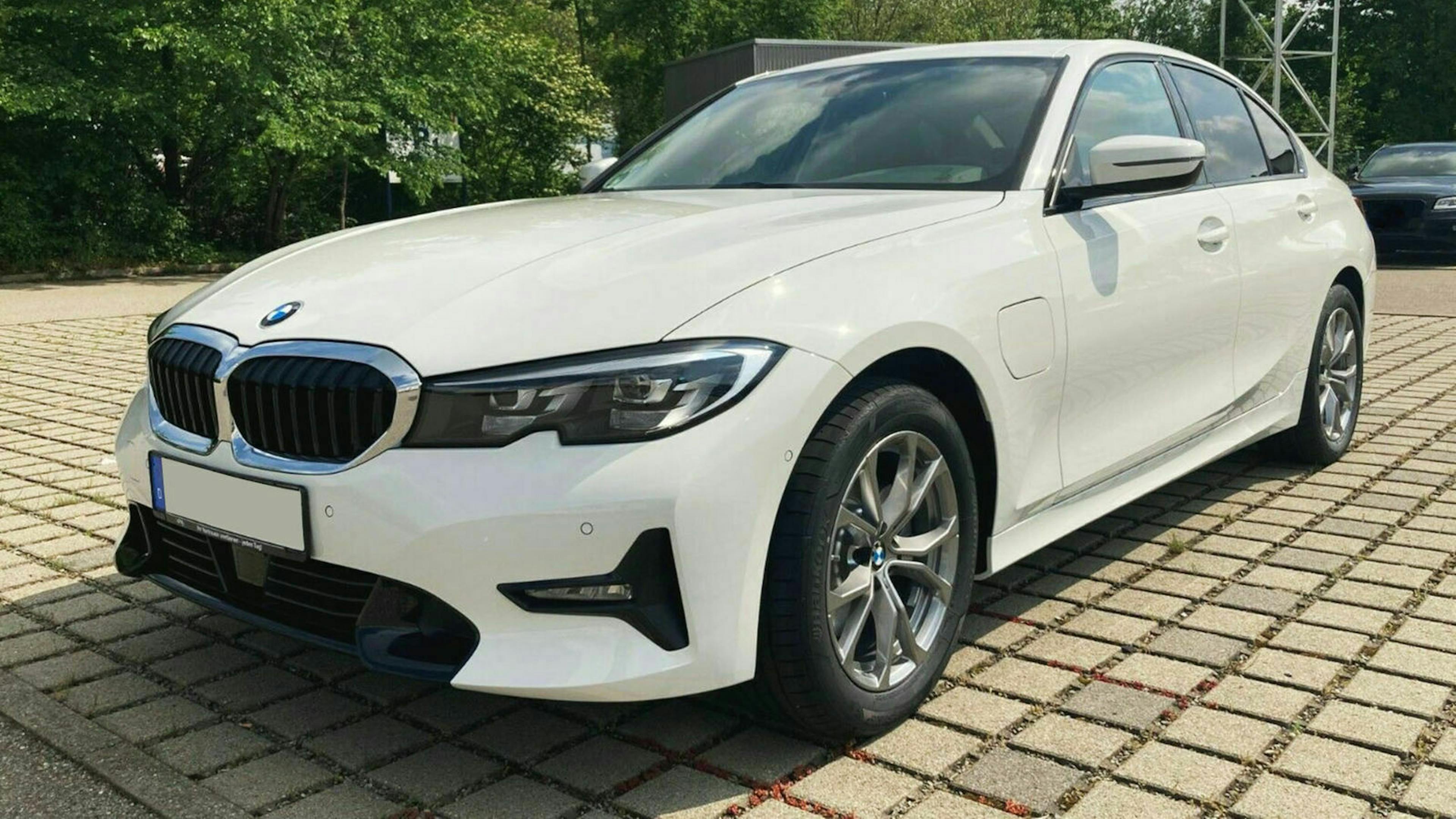 Ein weißer BMW 320e Touring steht auf einem Parkplatz vor einem Baum