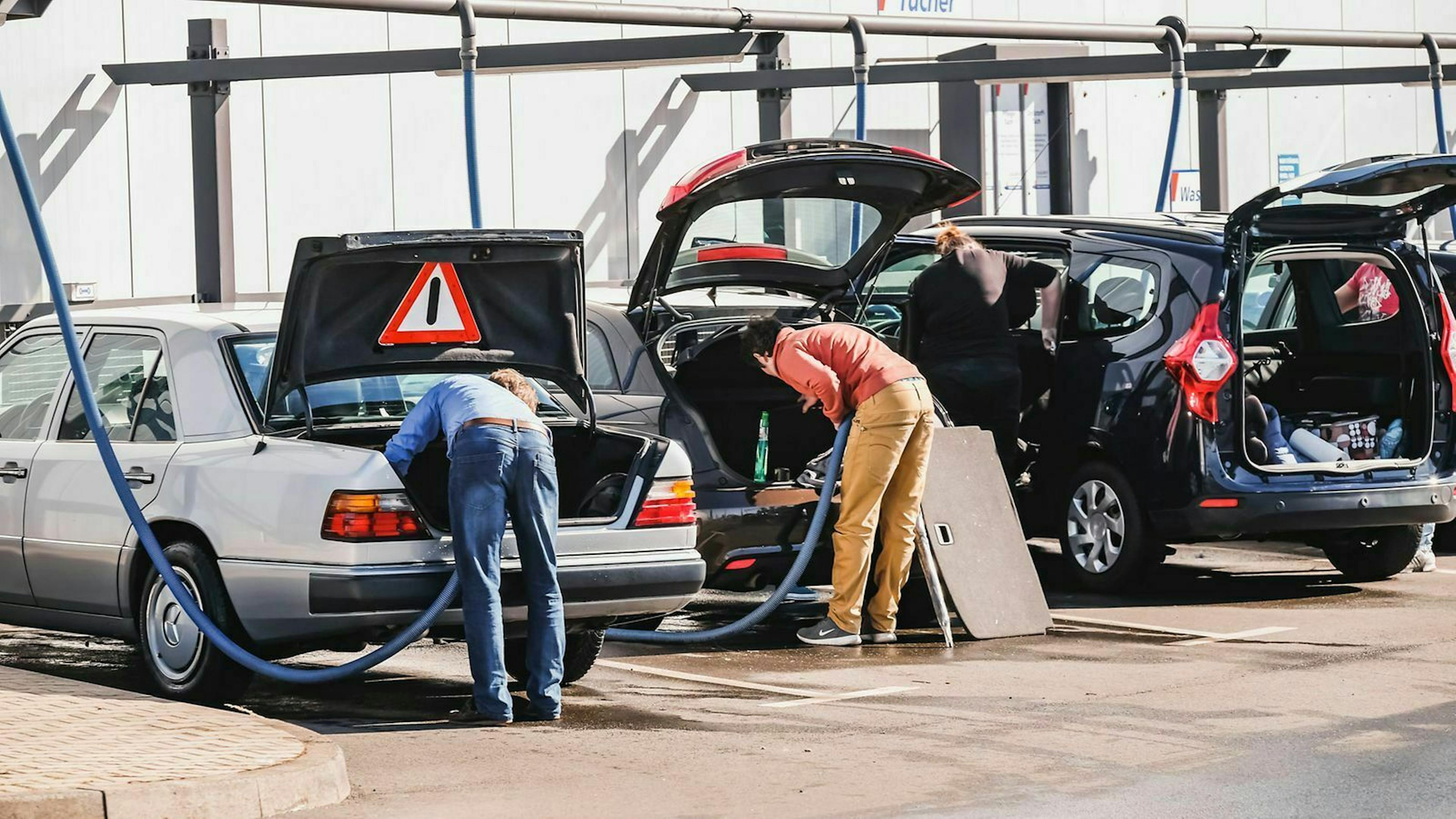 Drei Autos stehen mit geöffneter Kofferraumklappe an Stationen mit Autosaugern
