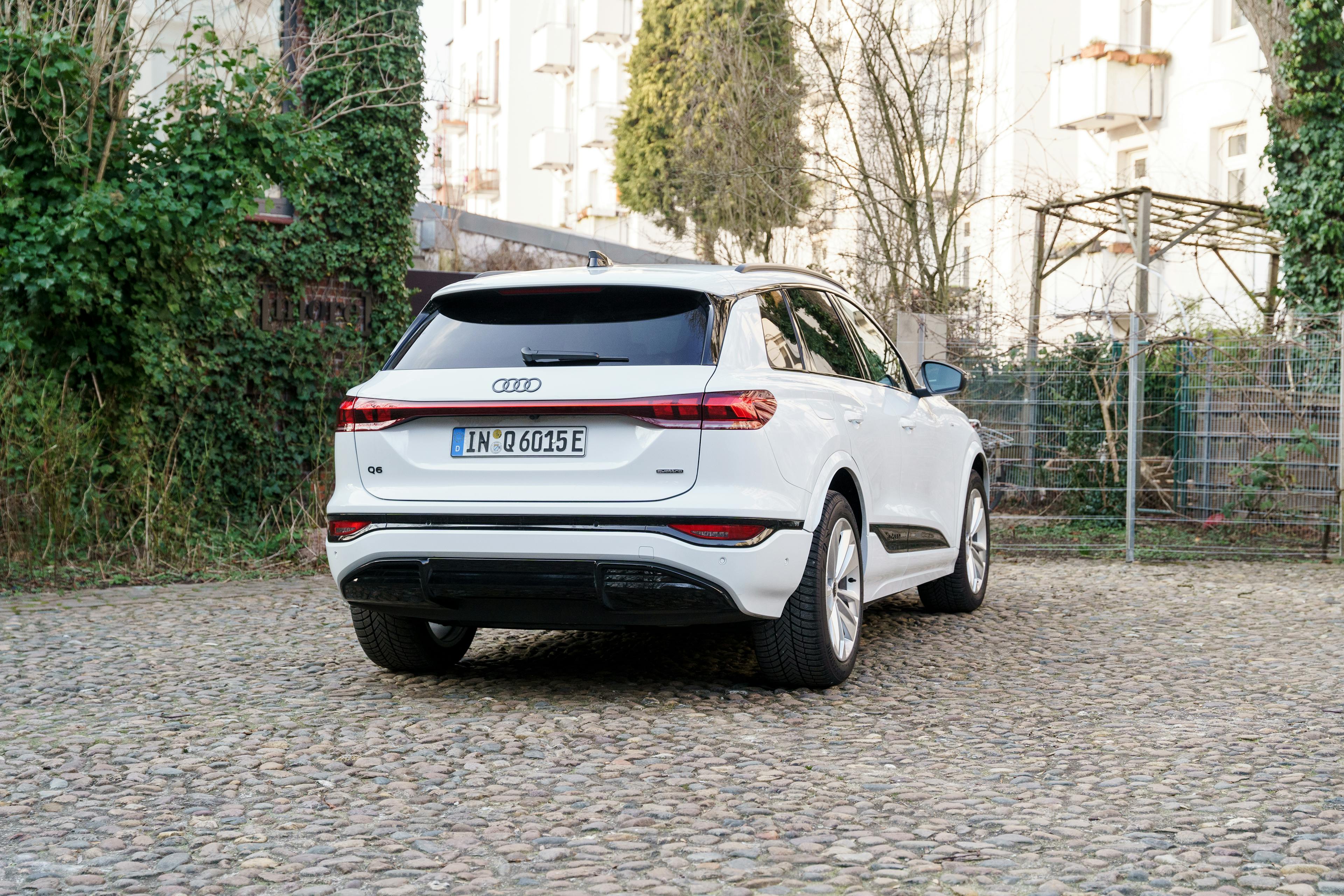 Die Heckansicht eines weißen Audi Q6 e-tron quattro auf einem Kiesplatz.