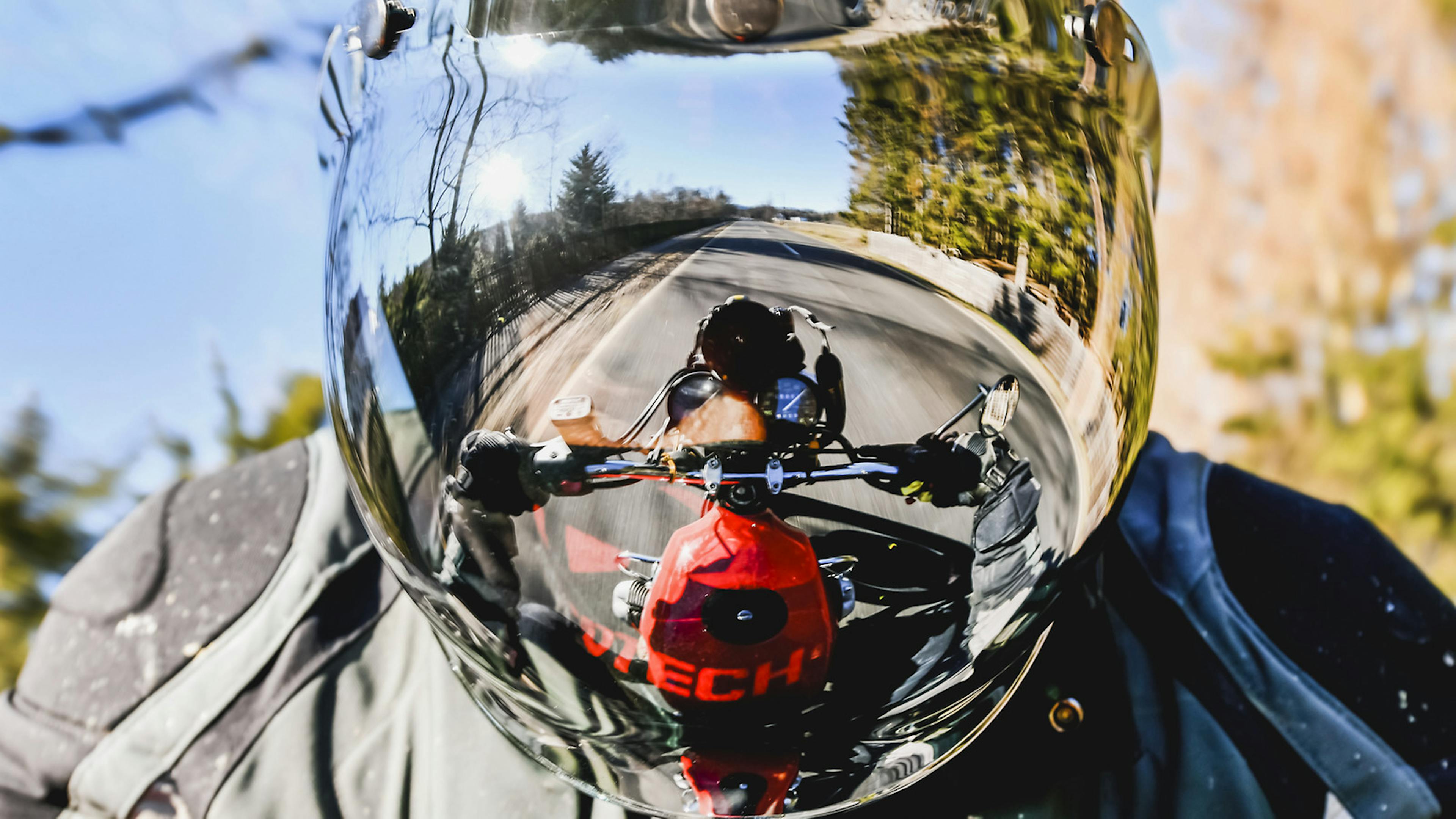 Ein Motorradlenker spiegelt sich im Visier eines Motorradhelms