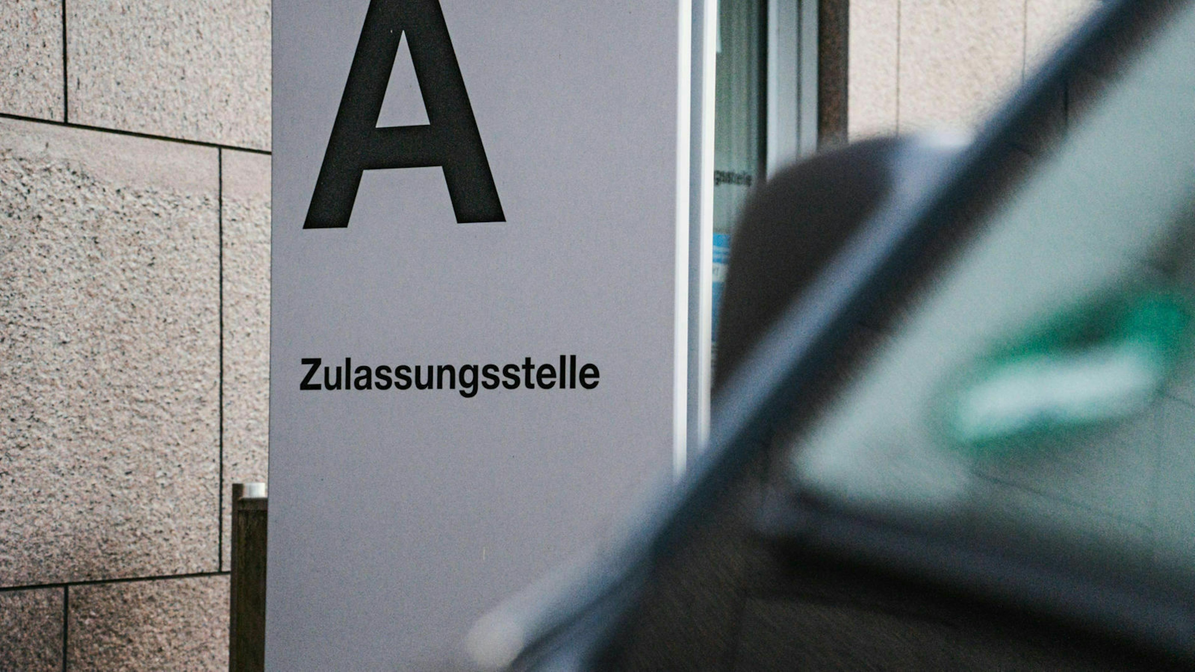 Auf einer Stele vor einem Verwaltungsgebäude und dem Gebäudeteil "A" steht "Zulassungsstelle"