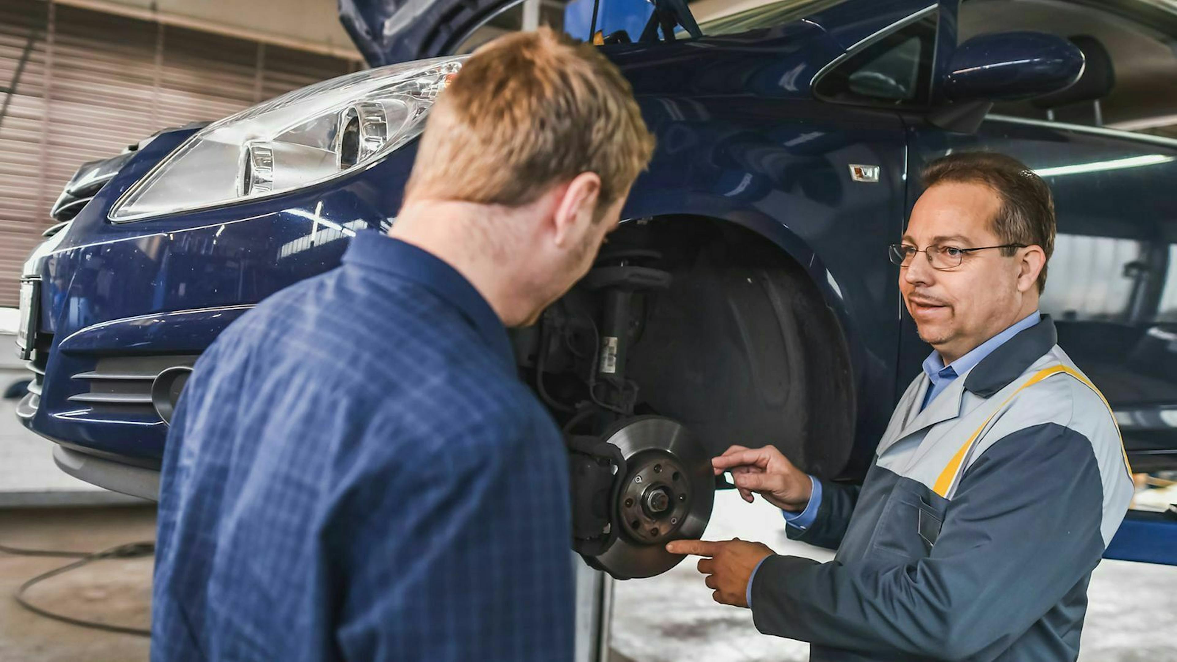 Ein Mechaniker zeigt auf die Bremsscheibe am Auto eines Kunden. 
