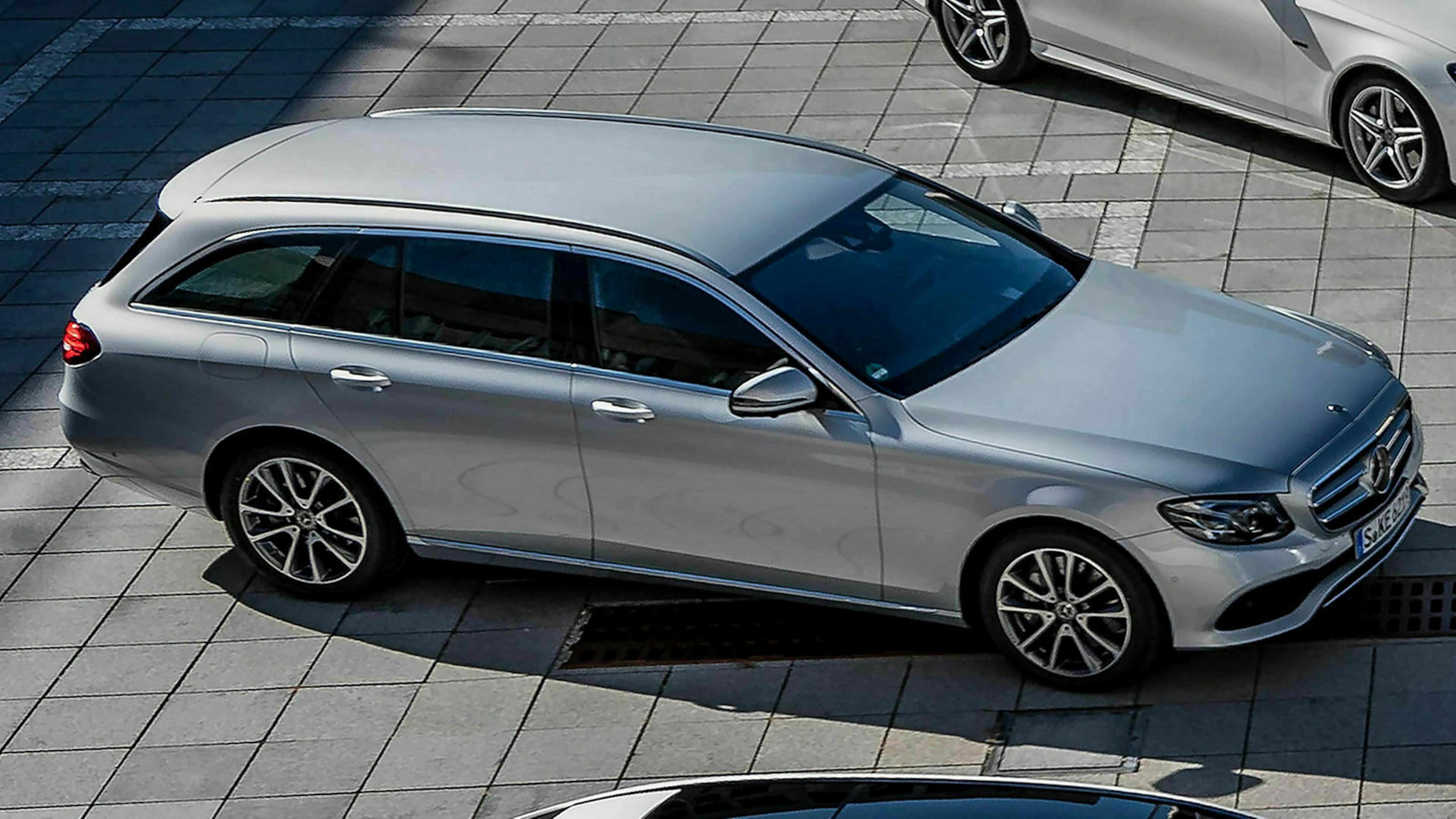 Ein silberner Mercedes-Benz E 300de parkt zwischen zwei anderen Mercedes-Modellen auf einem großen Parkplatz
