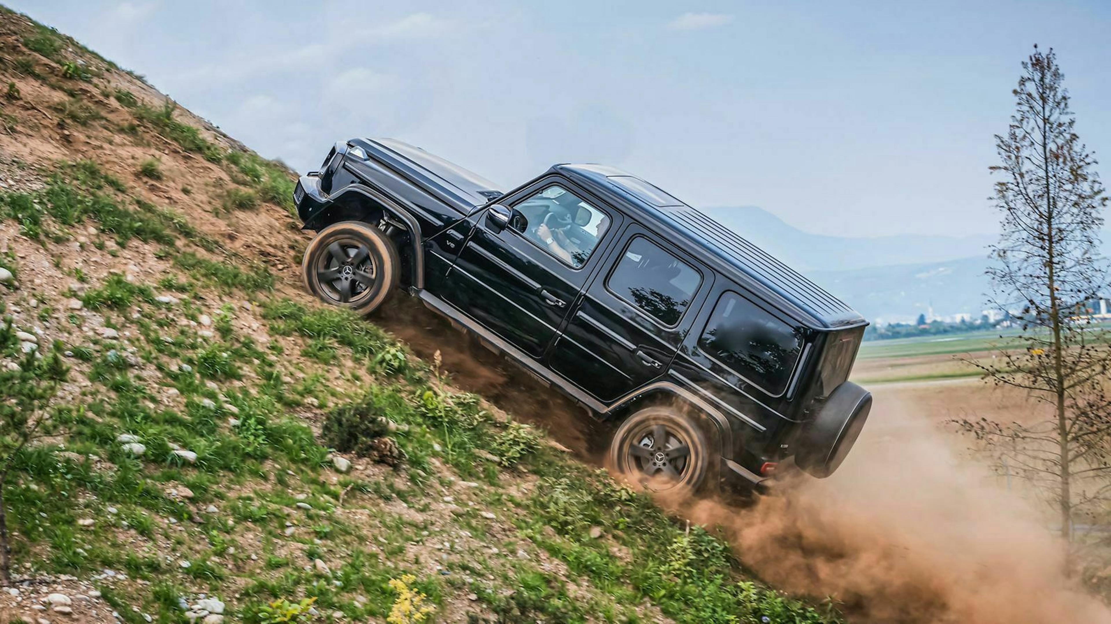 Eine schwarze Merecedes-Benz G-Klasse fährt Staub aufwirbelnd einen Hang hinauf.