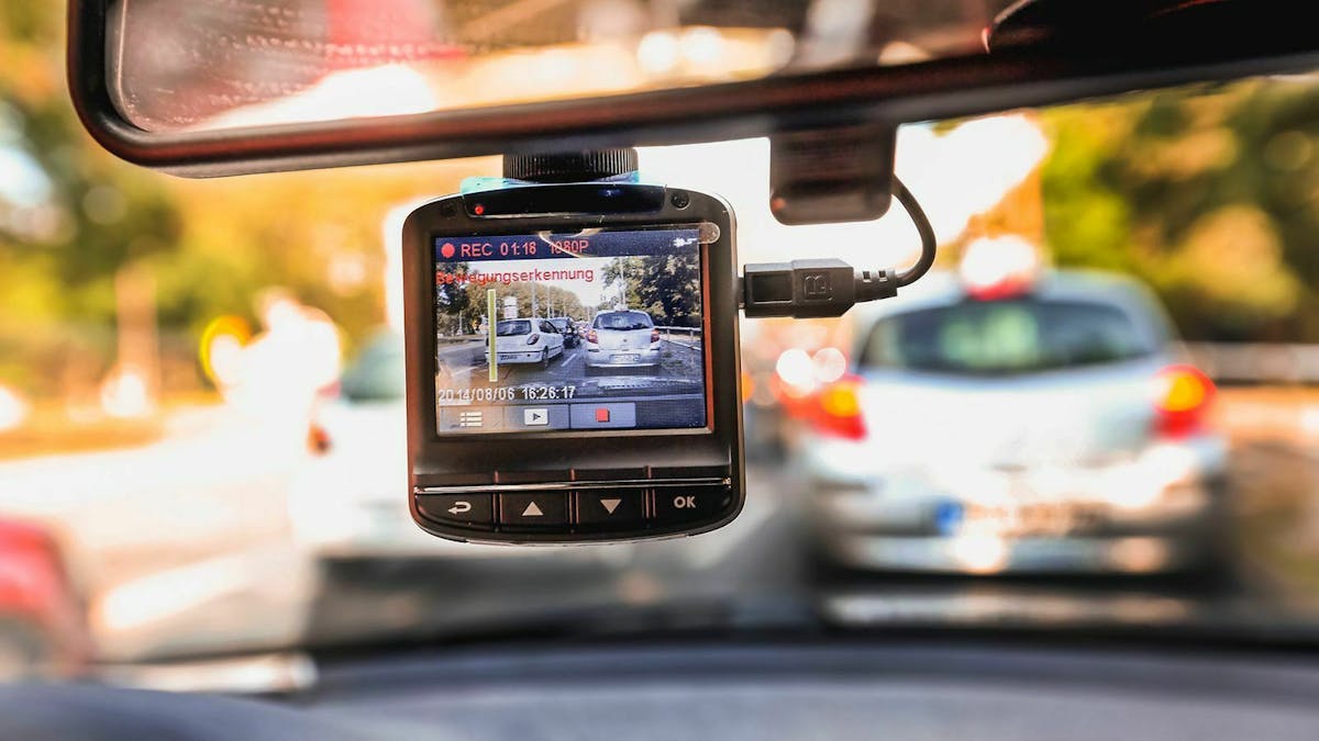 Im Vordergrund hängt eine Dashcam, im Hintergrund sind unscharf vorausfahrende Autos zu erkennen.