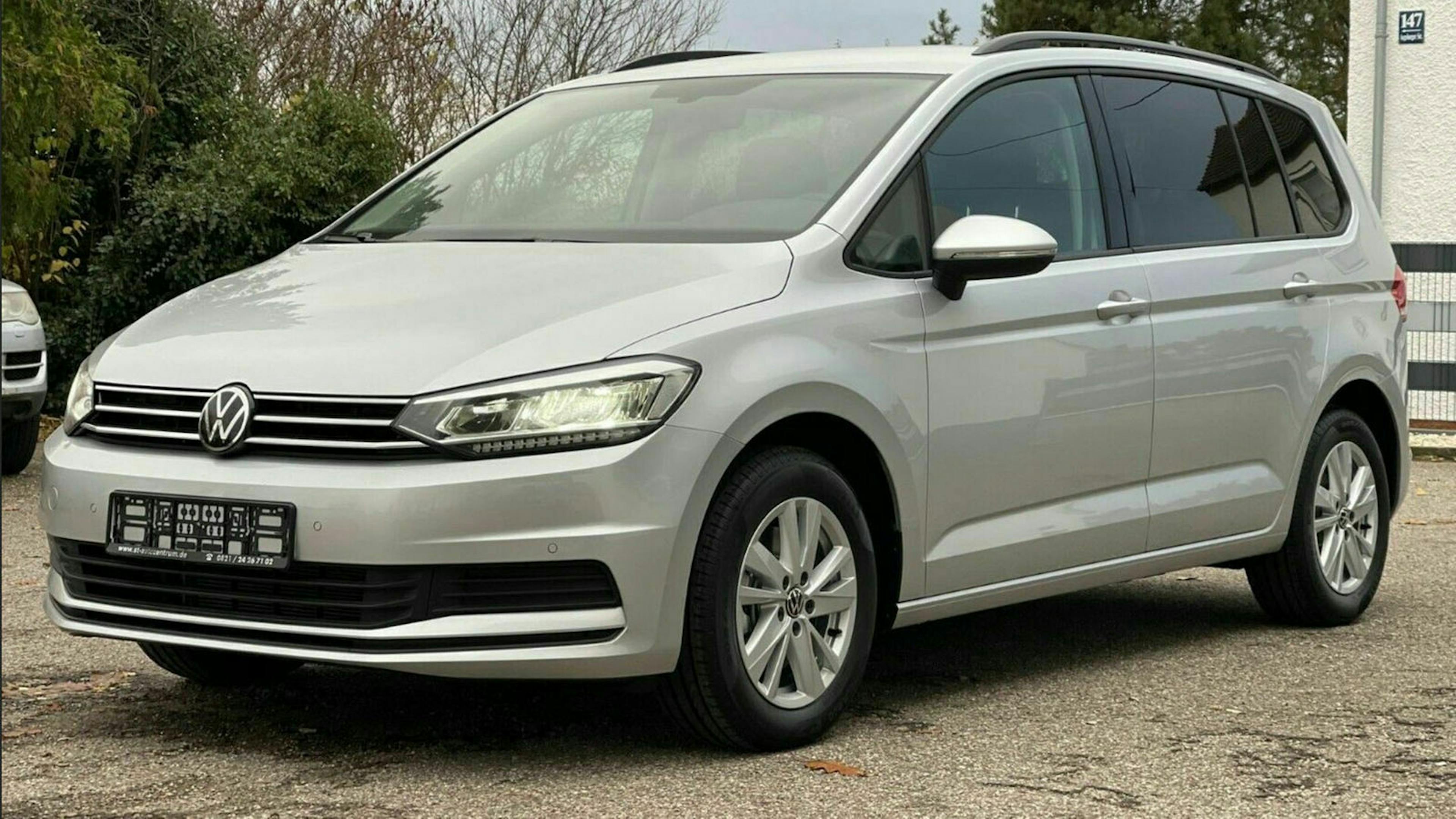 Ein grauer VW Touran steht auf einem Parkplatz vor einer weißen Wand