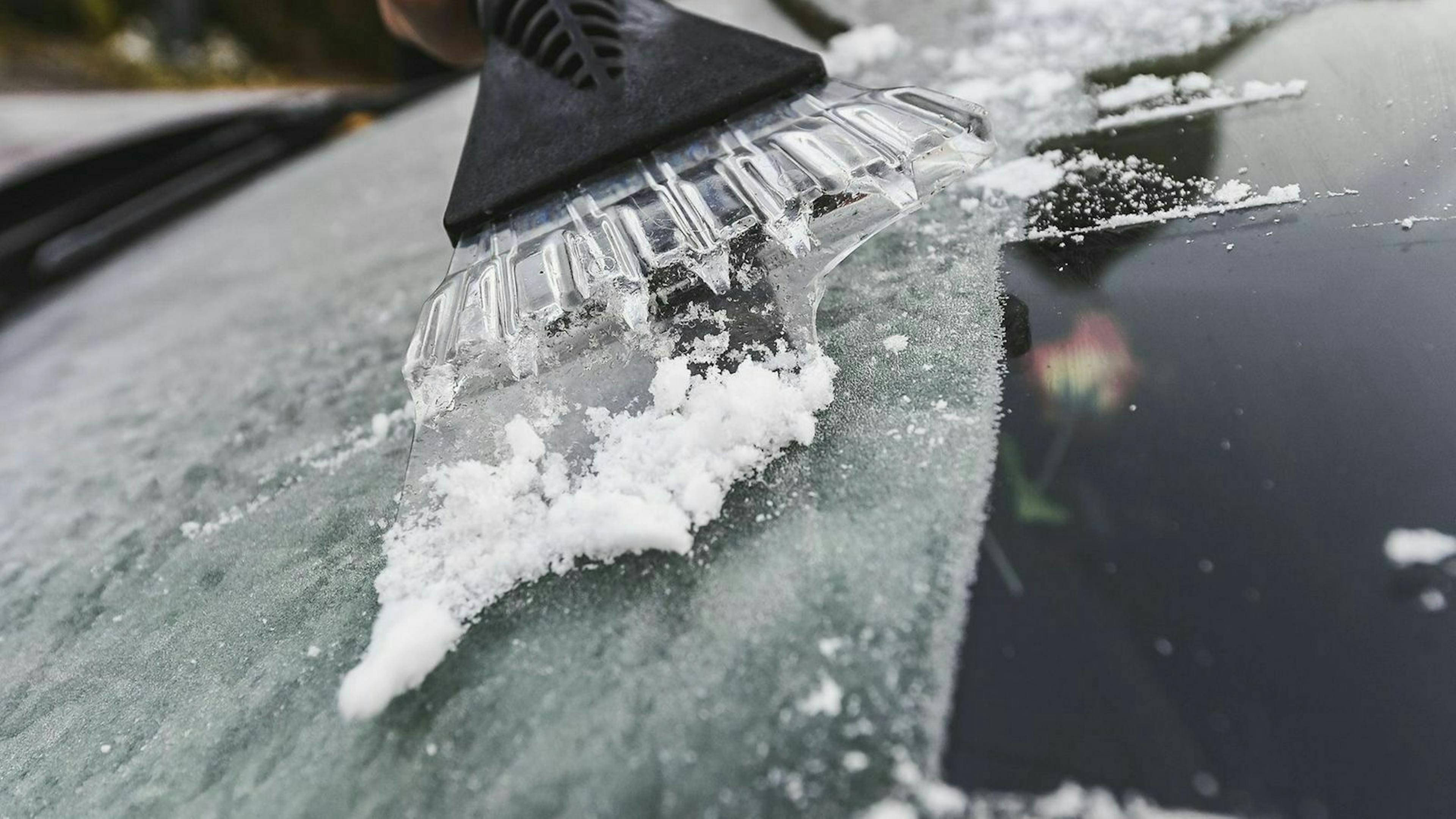 Eiskratzer an Fronstscheibe eines Autos 