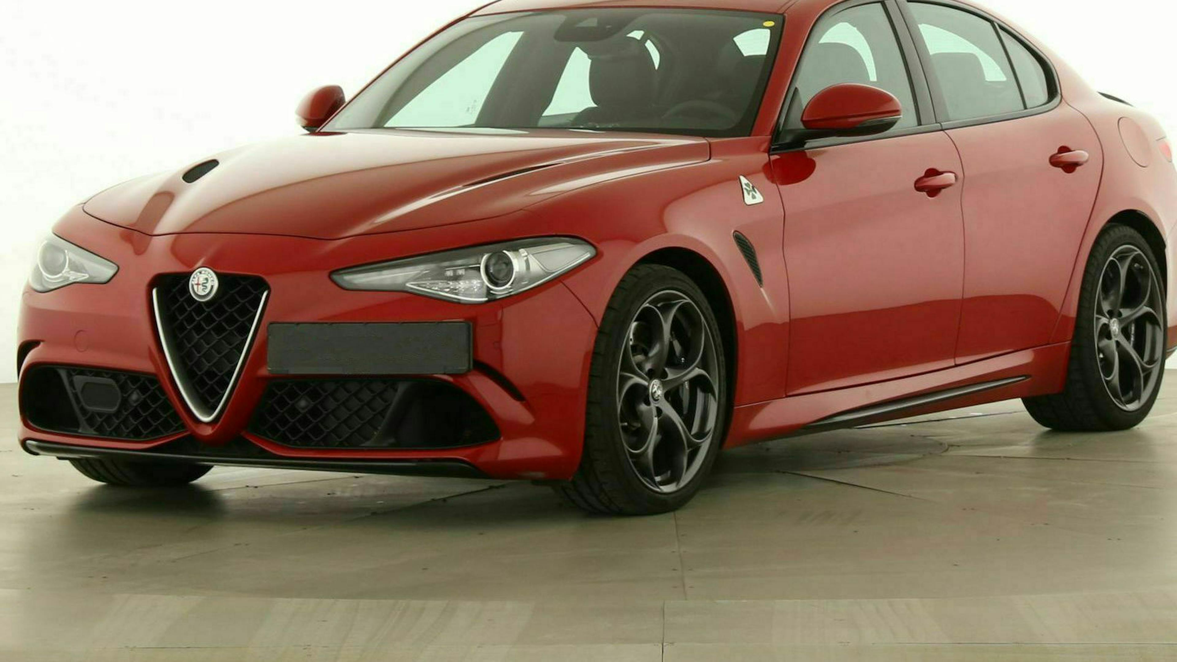 Eine rote Alfa Romeo Giulia mit Heckantrieb steht vor einer weißen Wand