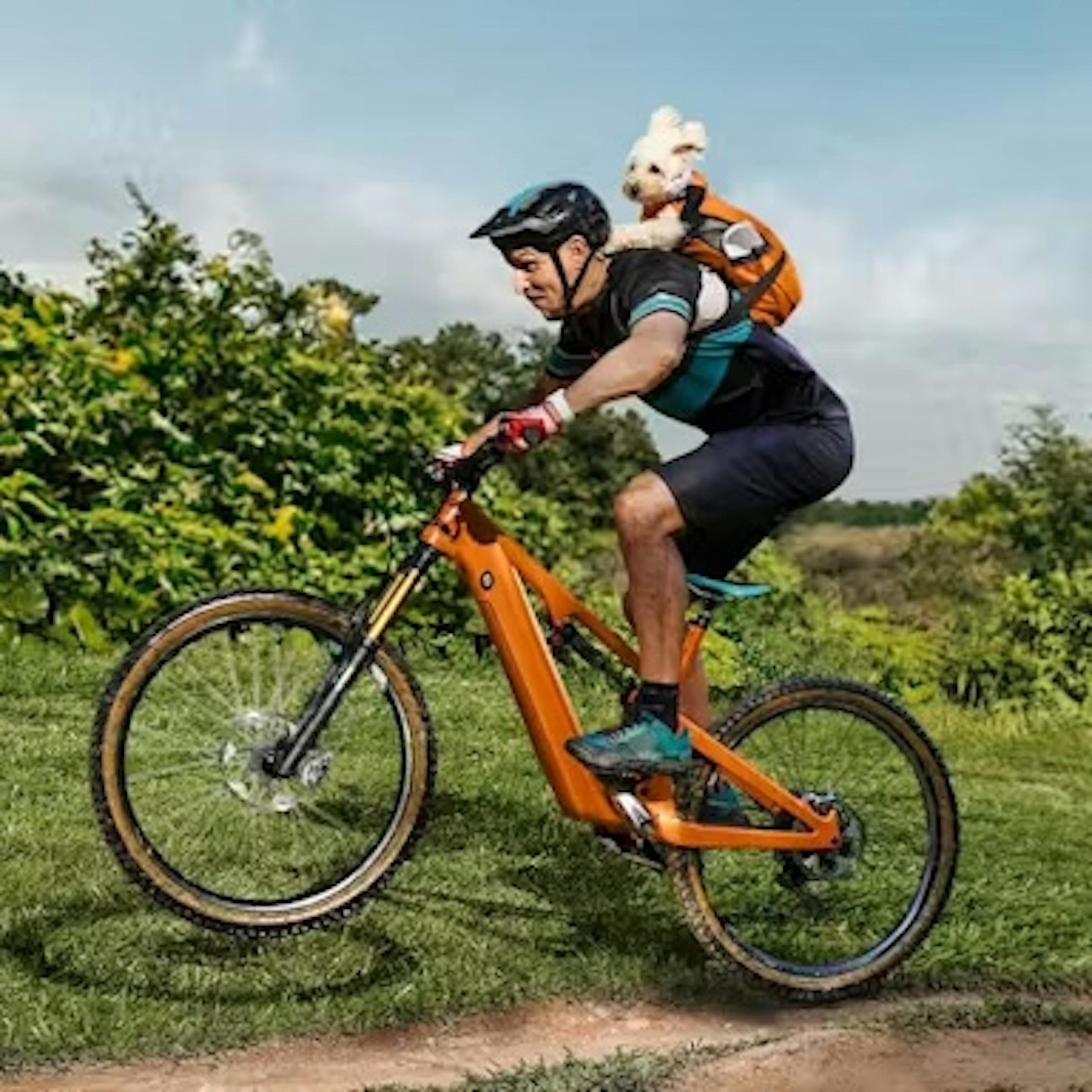 Ein Mann mit einem Hund auf dem Rücken fährt auf einem orangen E-Bike.