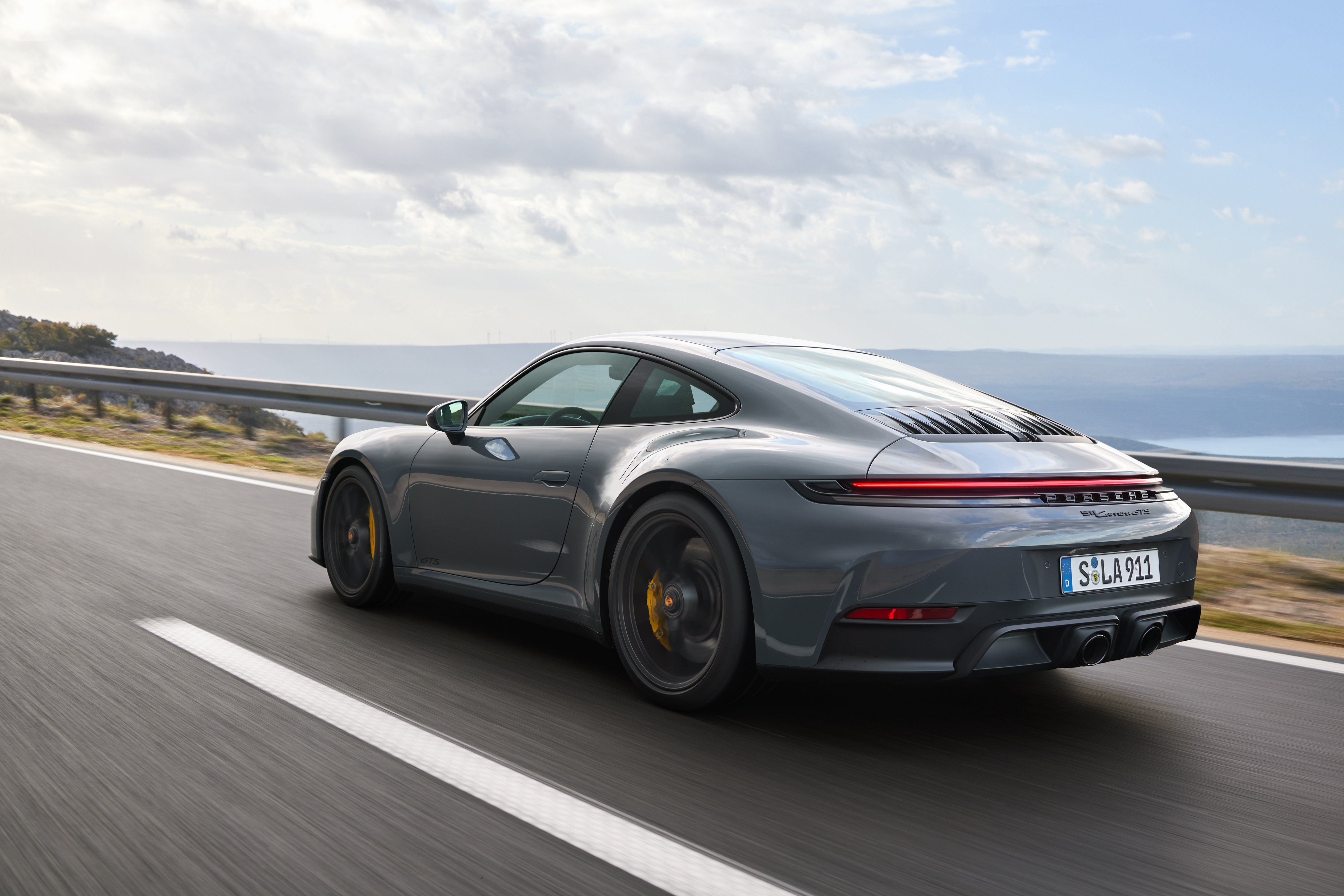 Ein grauer Porsche 911 2024 fährt auf einer Küstenstraße. 