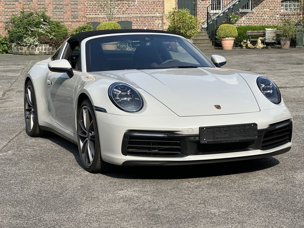 Ein weißer Porsche 911 (992) Cabrio parkt auf einem Hof. 