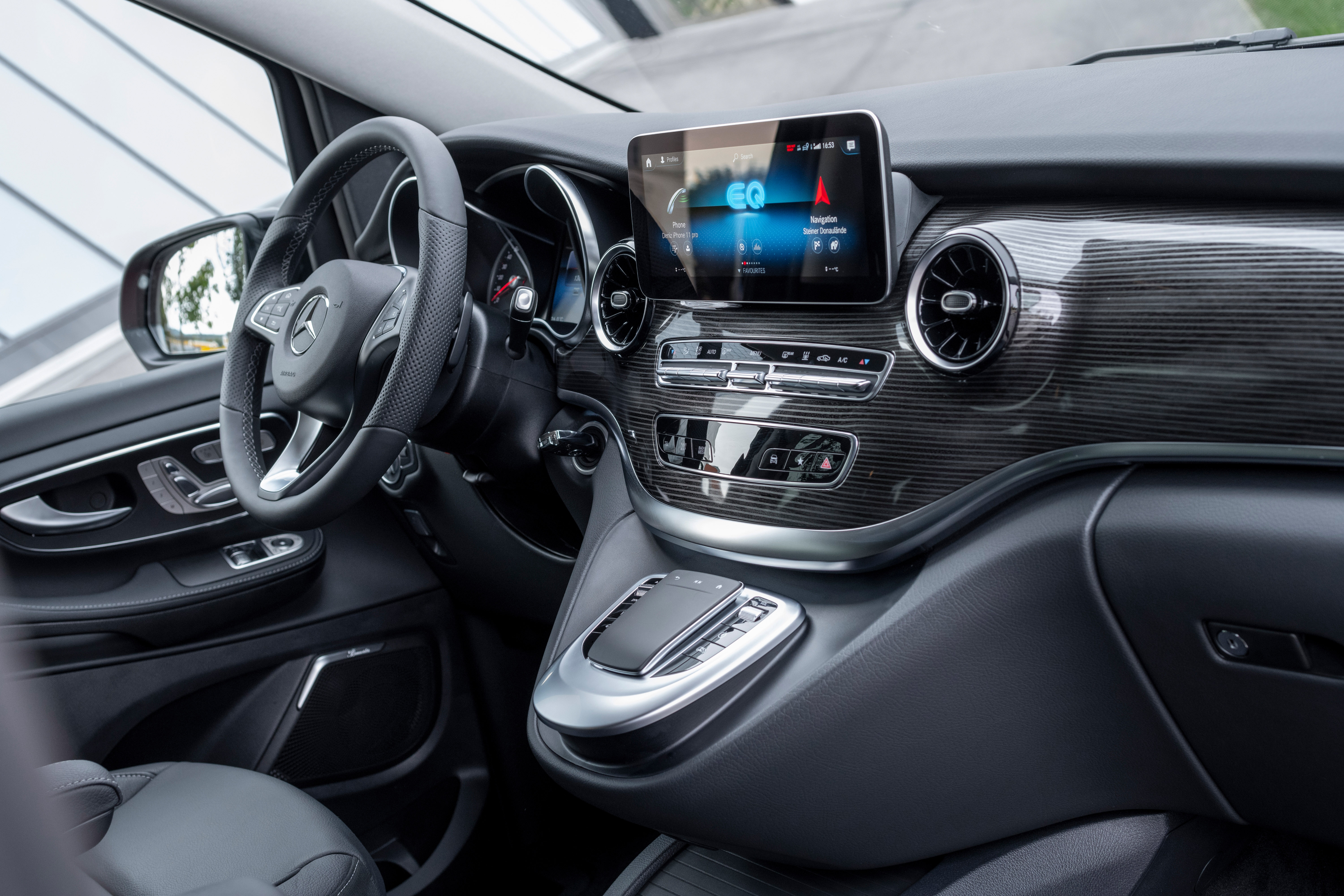 Modernes Auto-Interieur mit Lederlenkrad, Holzoptik-Armaturenbrett und digitalem Touchscreen-Display in der Mittelkonsole.