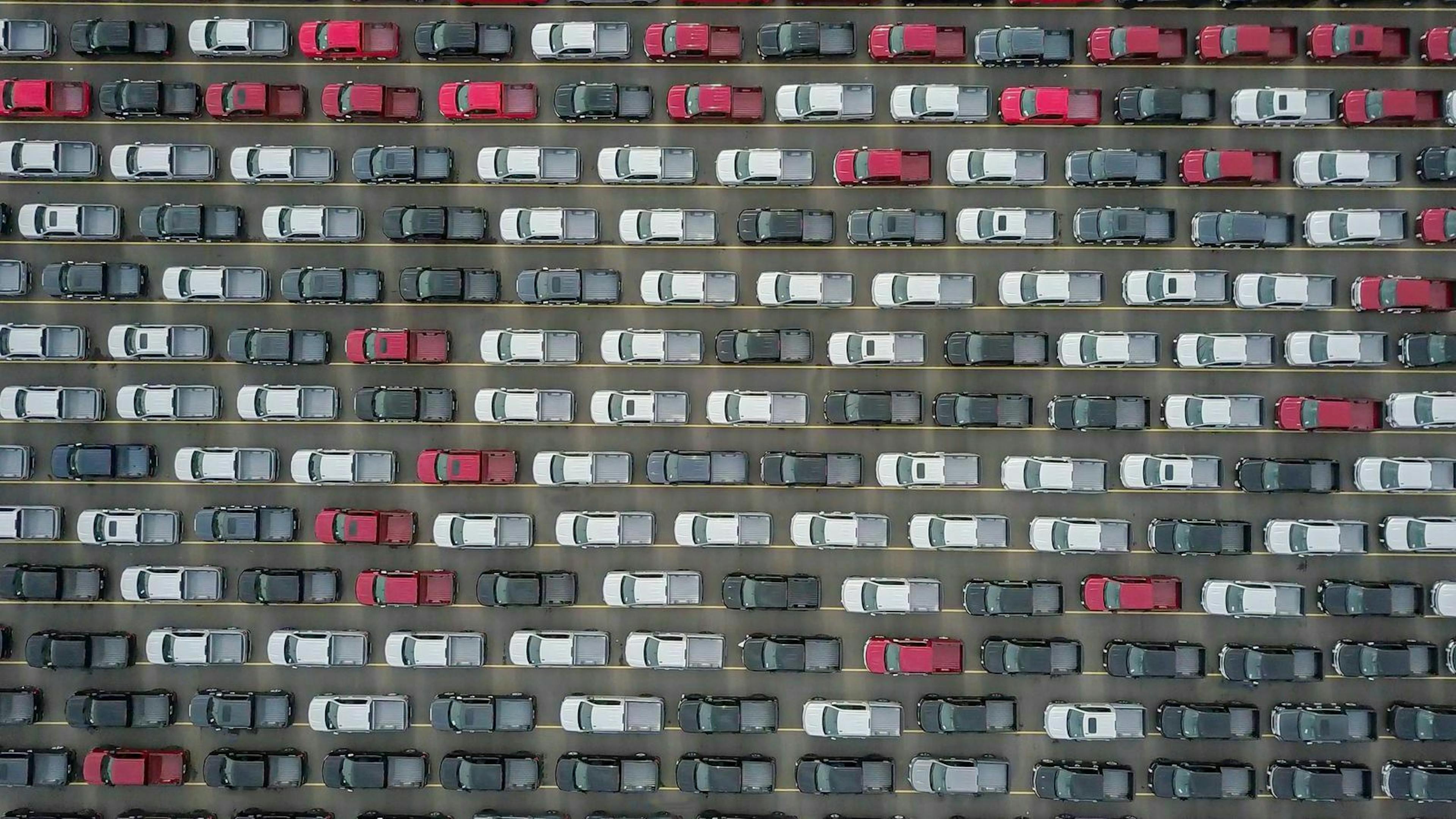 Luftaufnahme eines Platzes, auf dem rote, weiße, graue und schwarze Autos dicht an dicht stehen