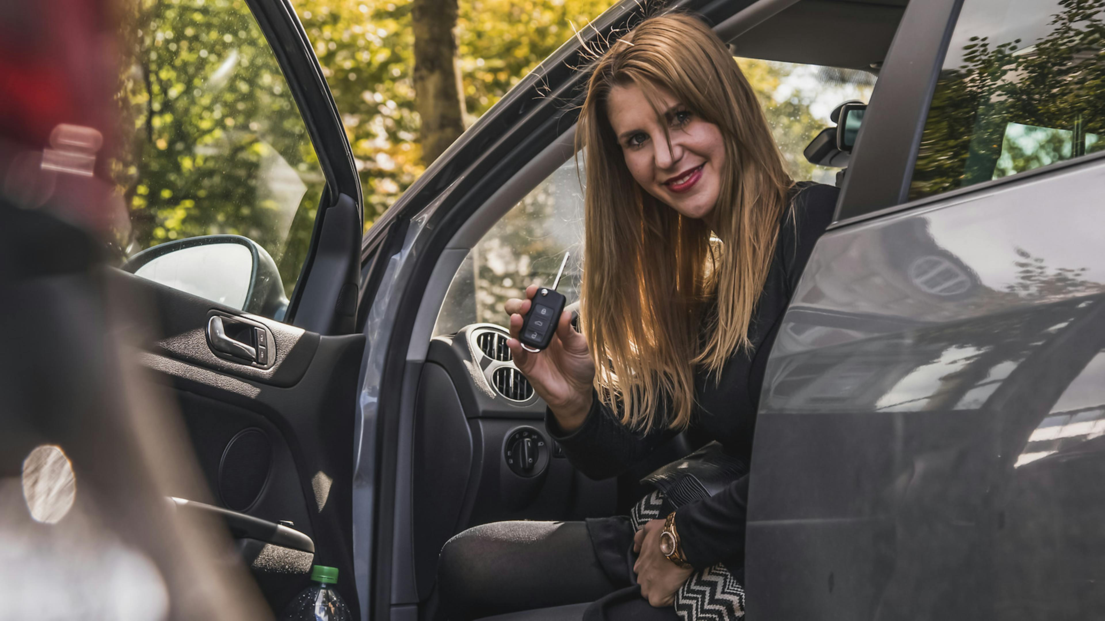 Jemand sitzt bei offener Autotür auf dem Fahrersitz und zeigt den Autoschlüssel.