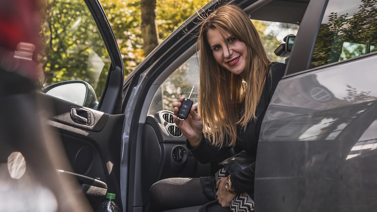 Jemand sitzt bei offener Autotür auf dem Fahrersitz und zeigt den Autoschlüssel.