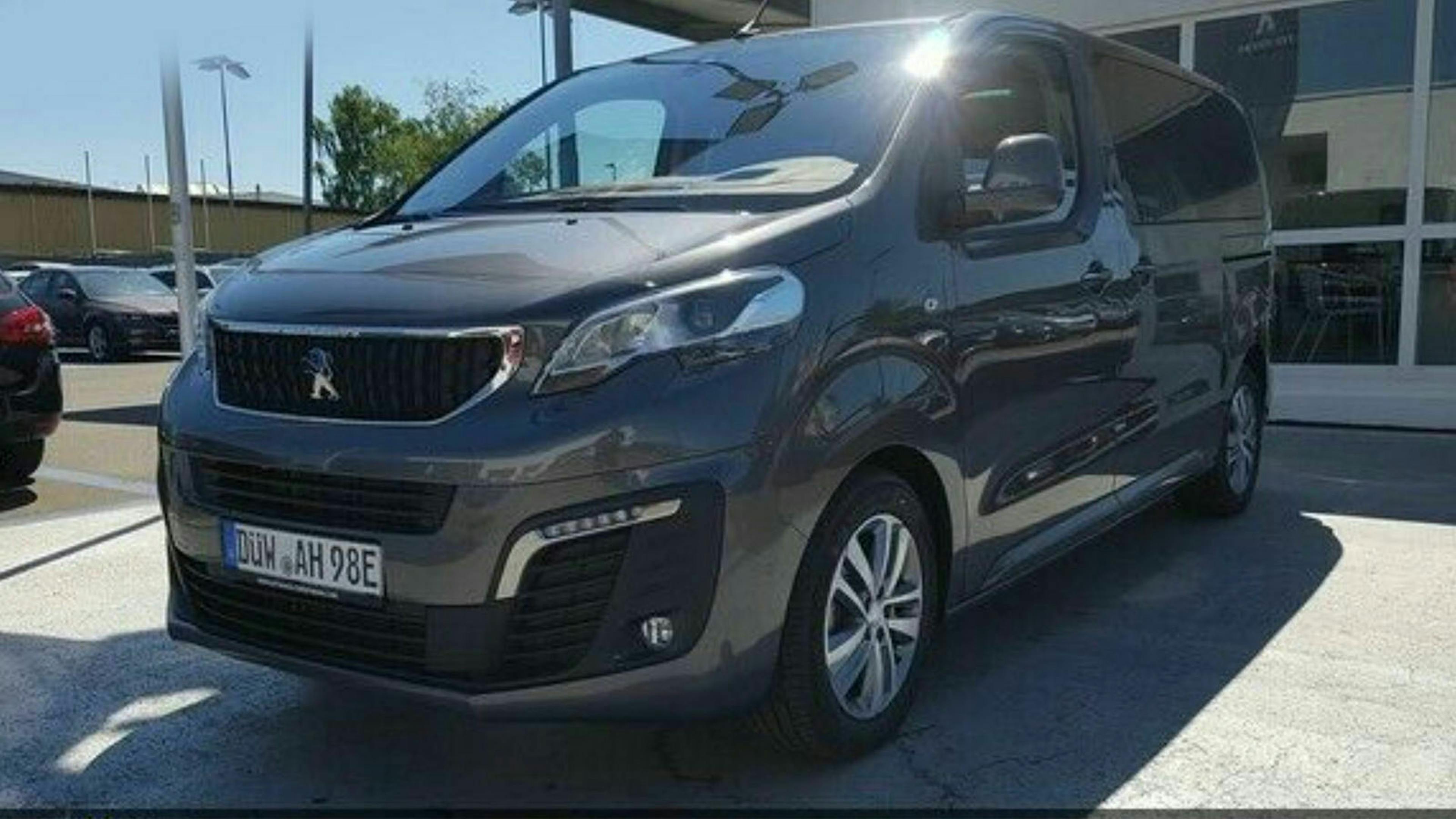 Ein dunkelgrauer Peugeot Traveller steht vor einem Gebäude auf einem Parkplatz