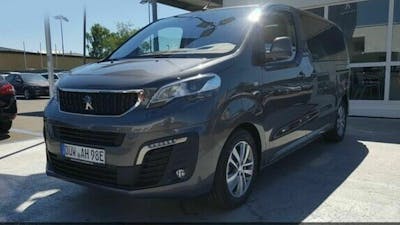 Ein dunkelgrauer Peugeot Traveller steht vor einem Gebäude auf einem Parkplatz