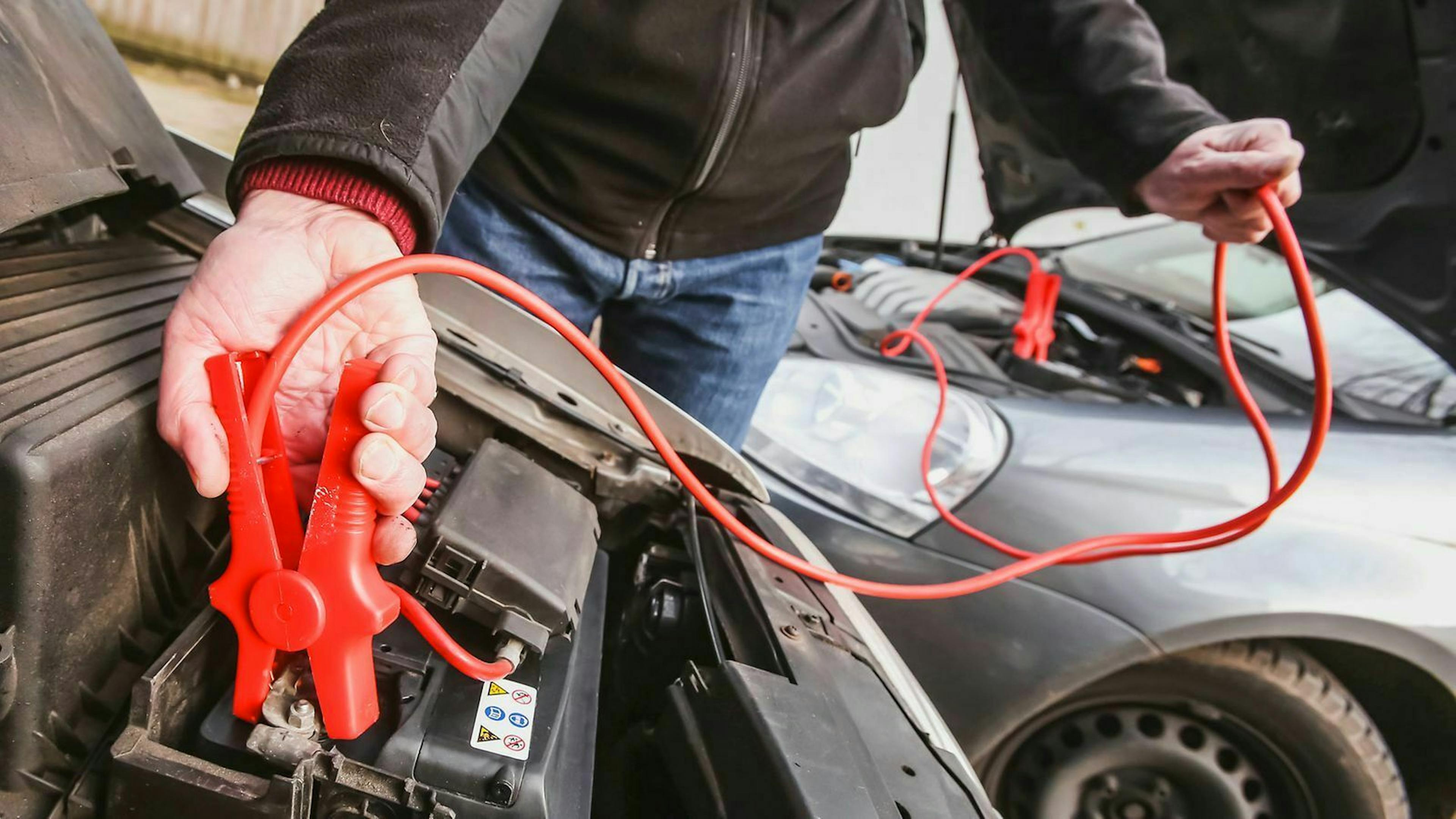 Jemand klemmt das rote Ende eines Starthilfekabels an eine Autobatterie.