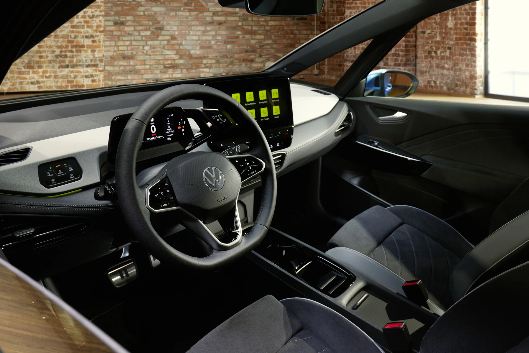 Modernes Auto-Interieur mit digitalem Cockpit, großem Touchscreen und schwarzer Polsterung, aufgenommen in einem Backsteinraum.
