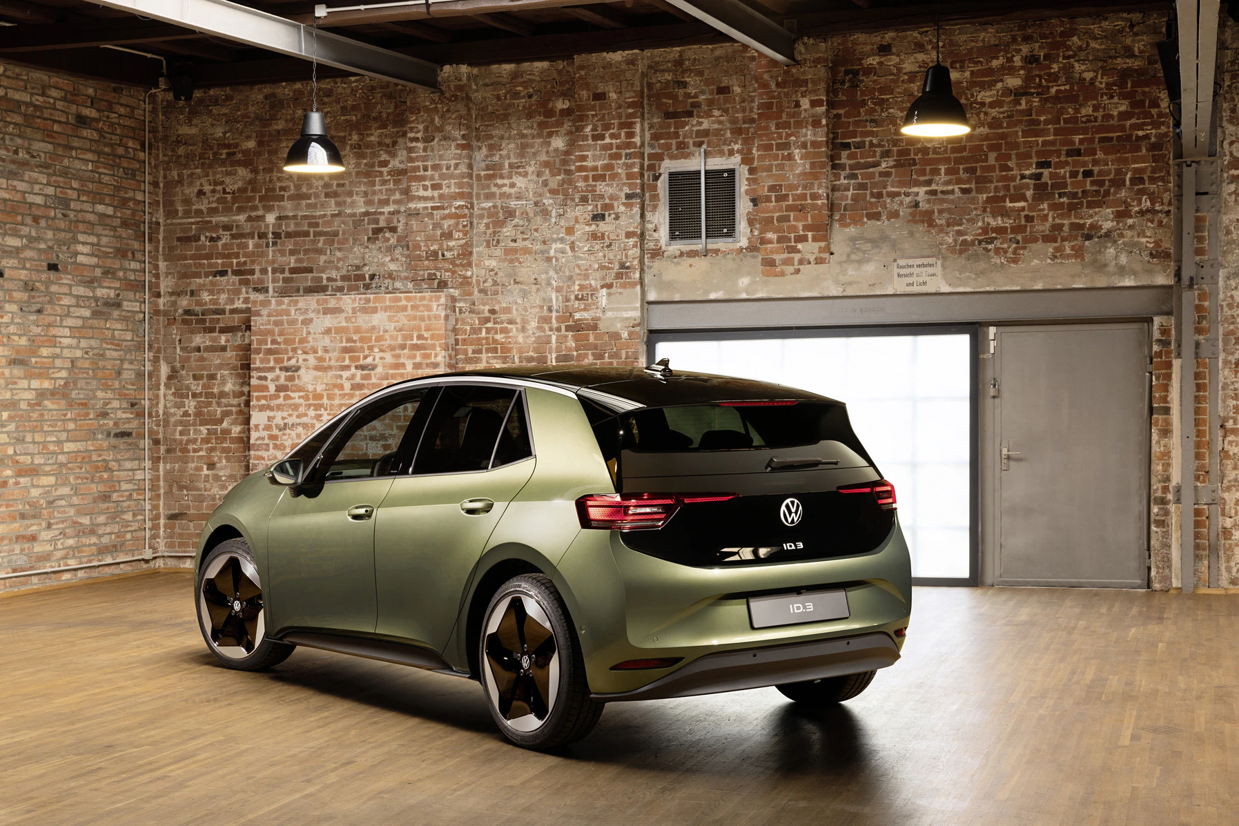 Ein grüner VW ID.3 steht in einem Loft mit Backsteinwänden und Holzfußboden, beleuchtet von Industrielampen.