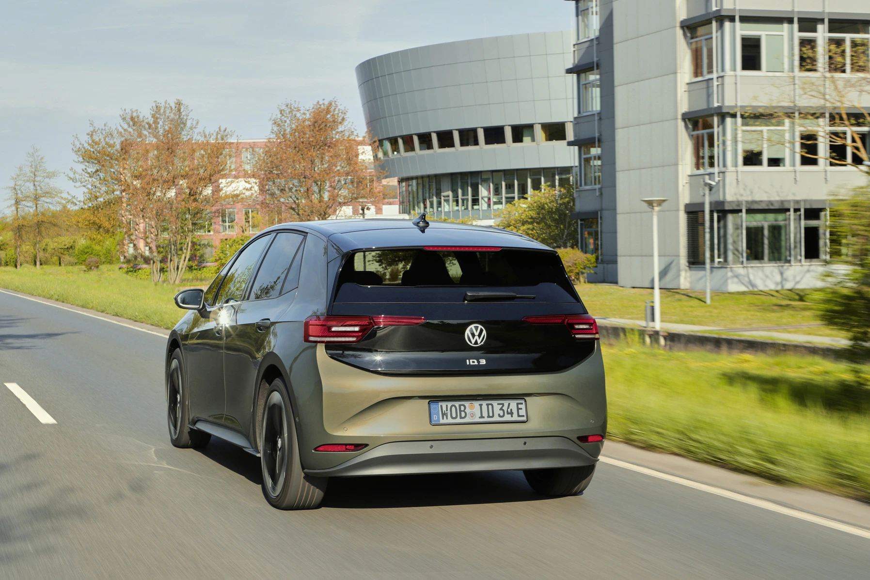 Ein Volkswagen ID.3 fährt auf einer Straße mit modernen Bürogebäuden im Hintergrund.