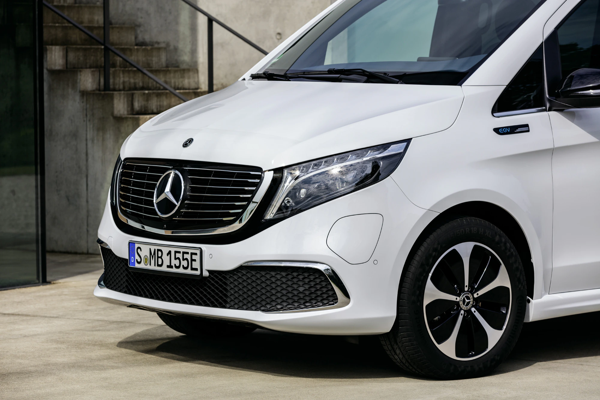 Weißer Mercedes-Benz EQV Elektro-Van, Frontansicht mit markantem Kühlergrill und Scheinwerfern, geparkt vor einer Betontreppe.