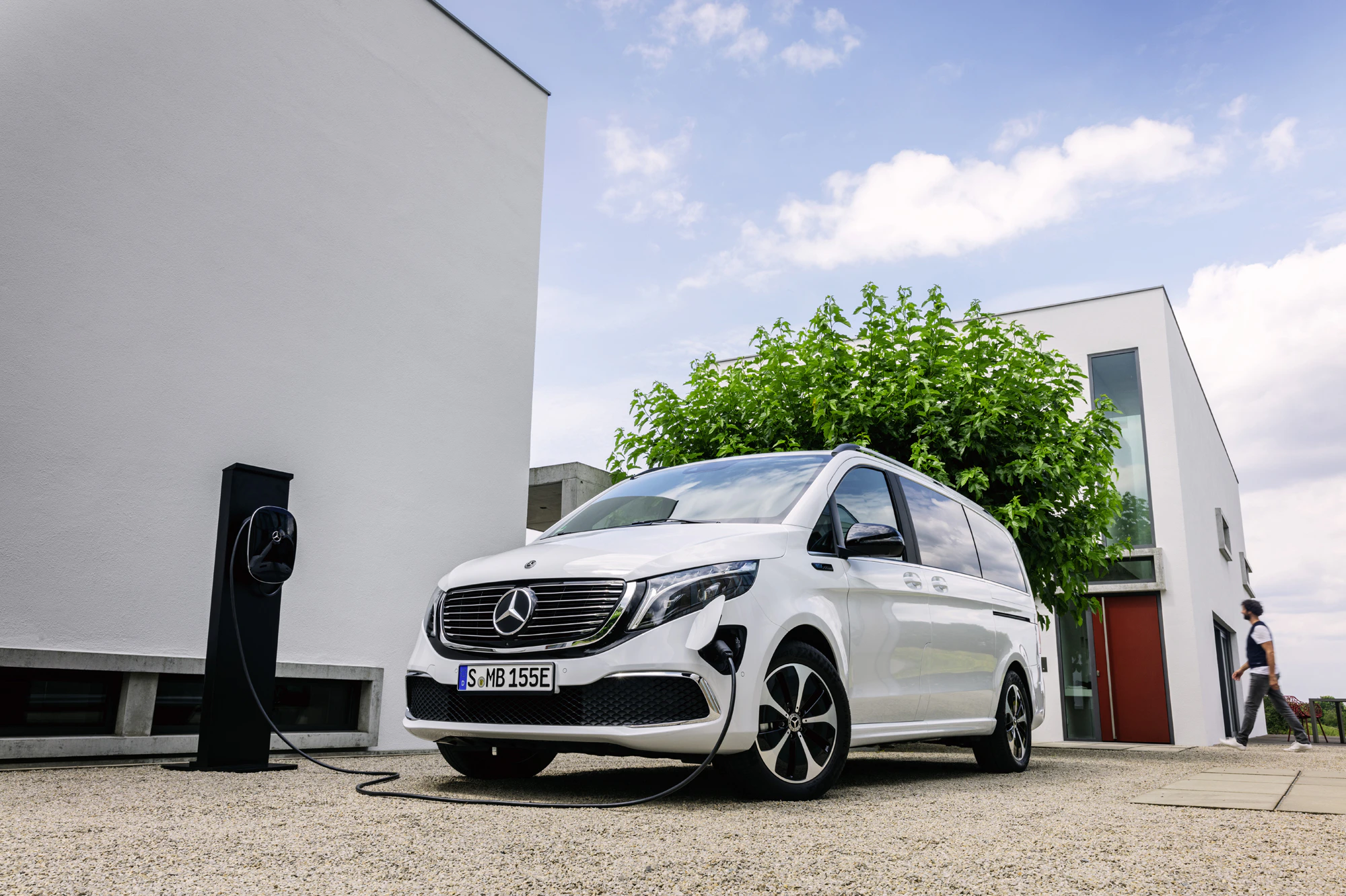 Weißer elektrischer Mercedes-Van lädt an einer Ladestation vor einem modernen Gebäude unter blauem Himmel.