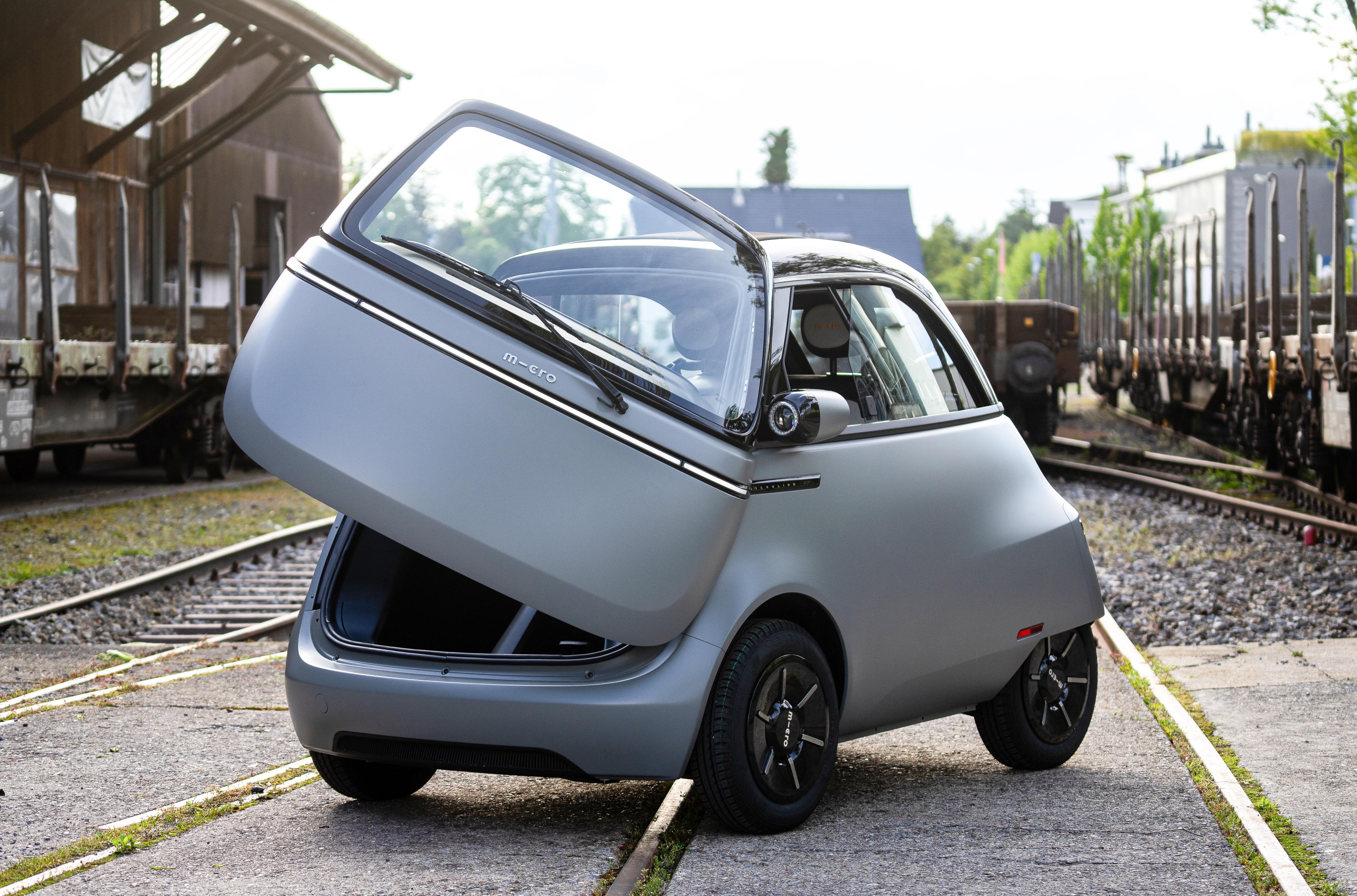 A gray Microlino is parked with the front door open