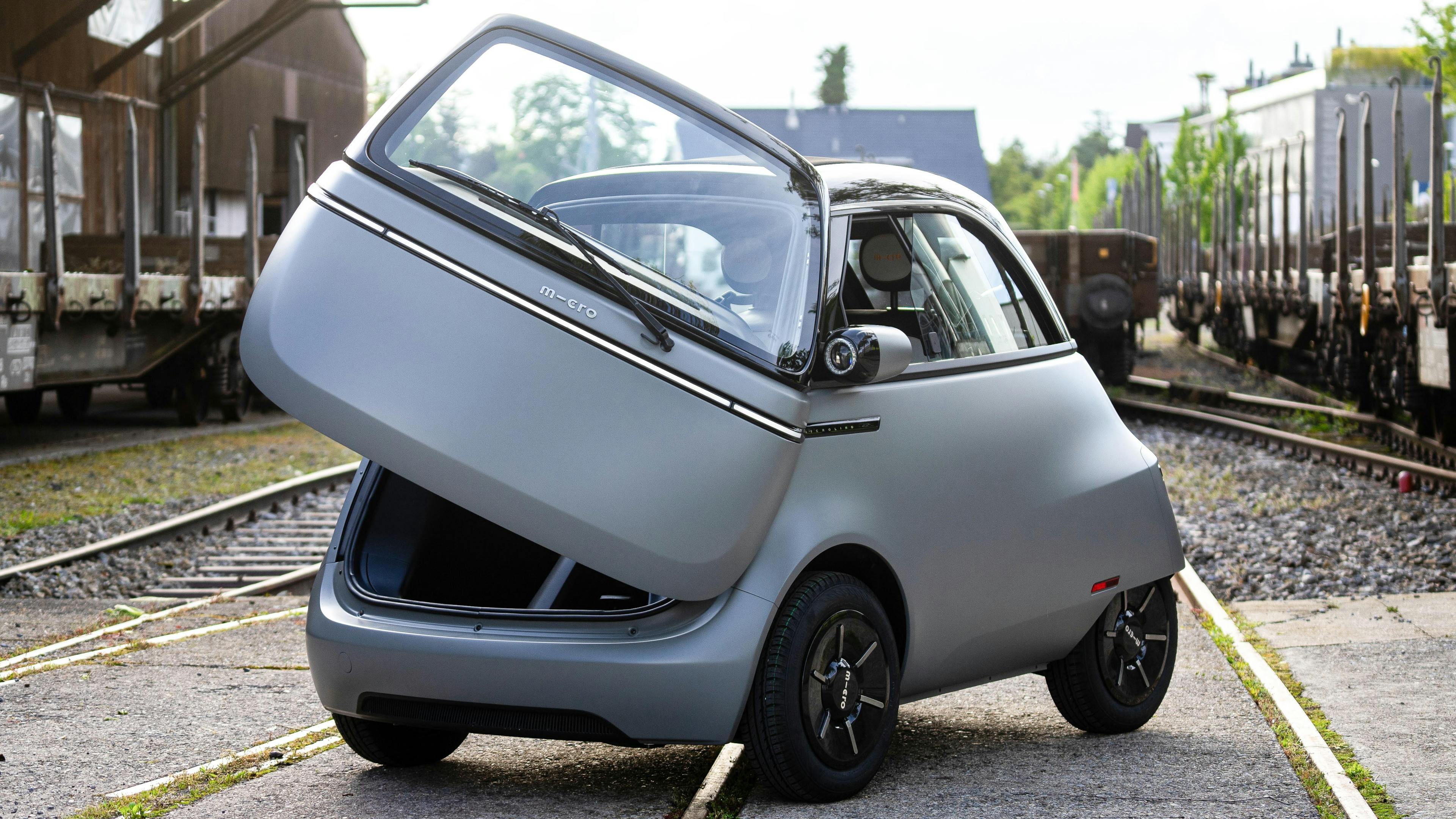 A gray Microlino is parked with the front door open