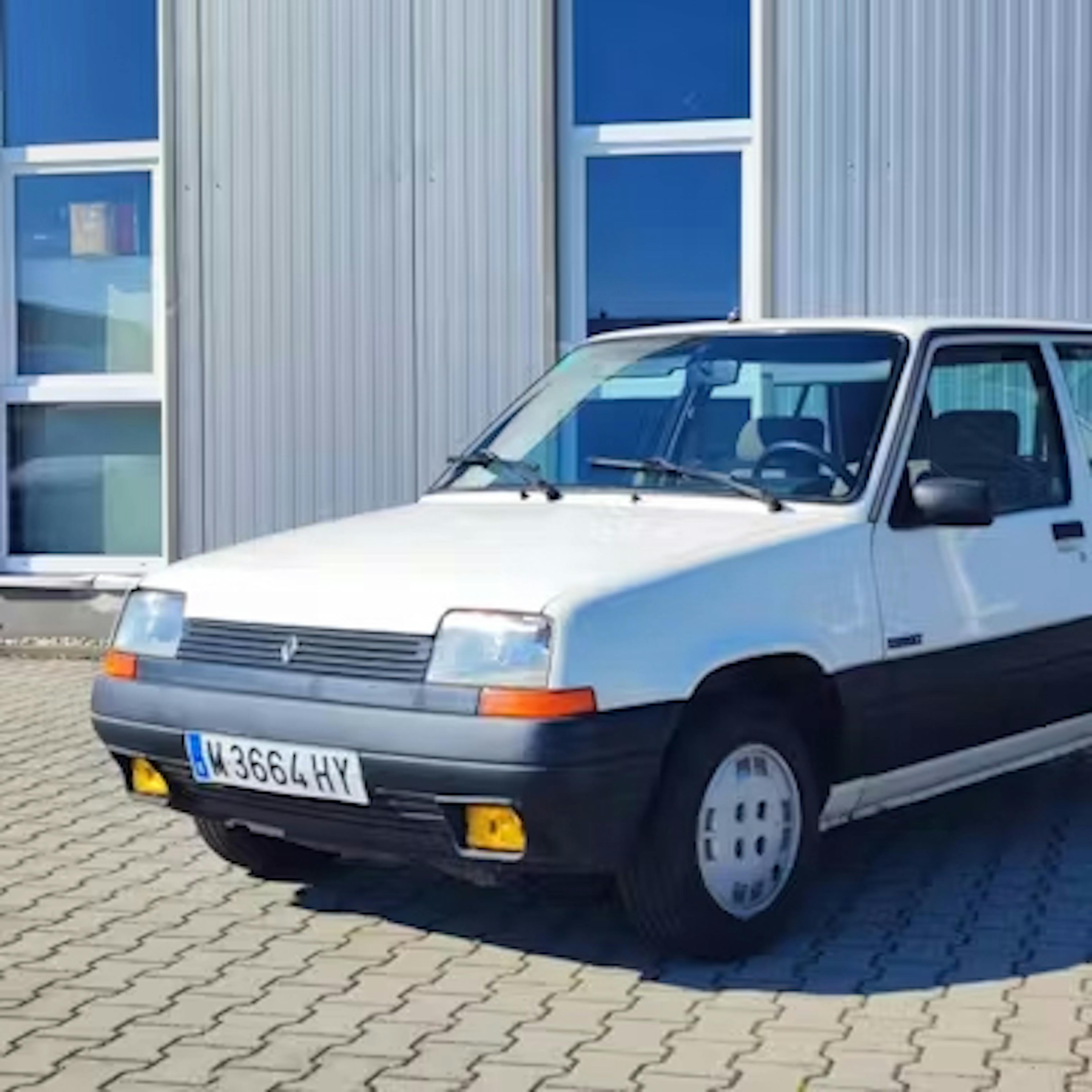 Ein weißer Renault 5 parkt for einem Industriegebäude.