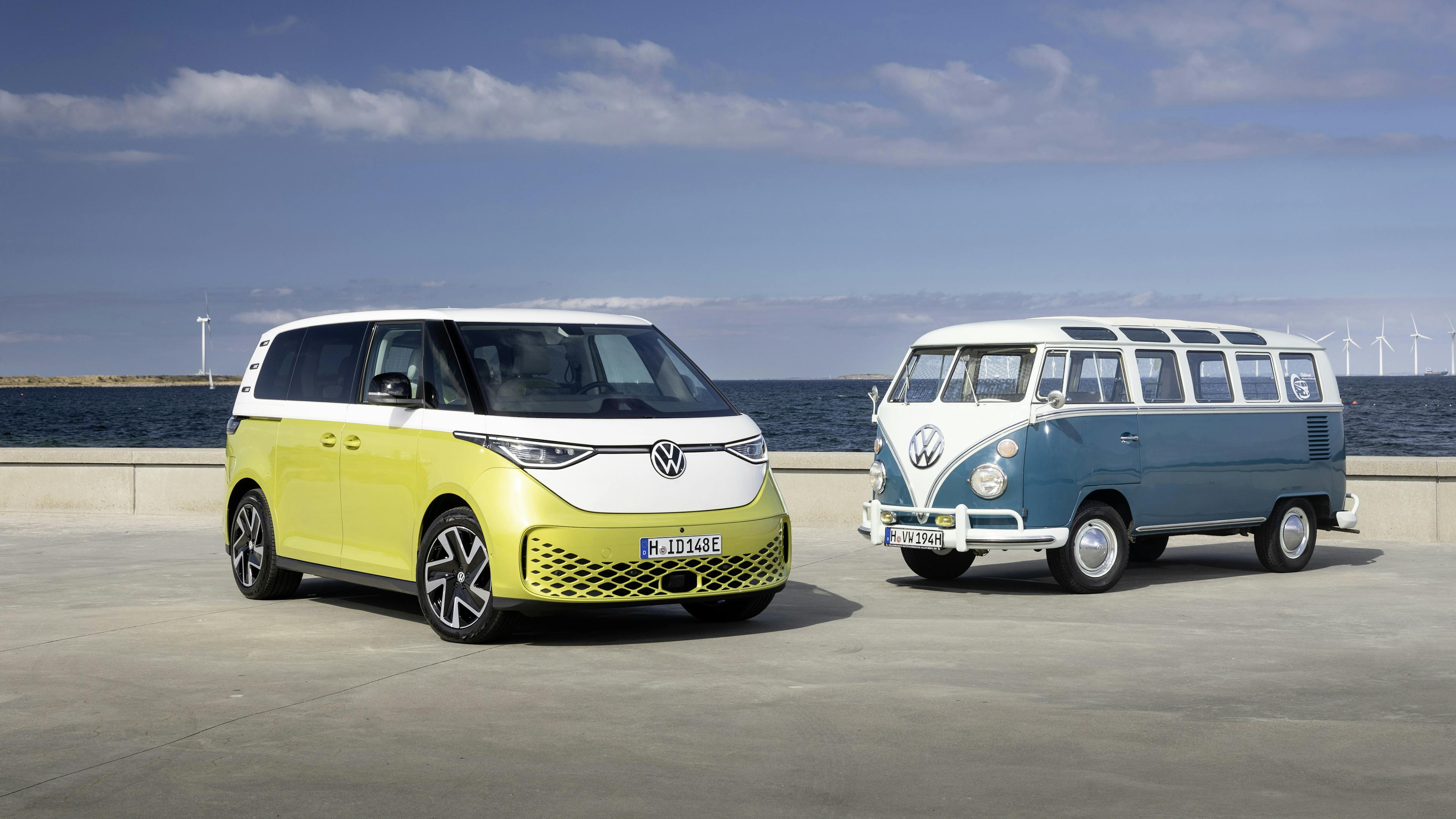 A yellow and white VW ID.Buzz and a blue and white VW Bulli are parked in a parking lot by the sea