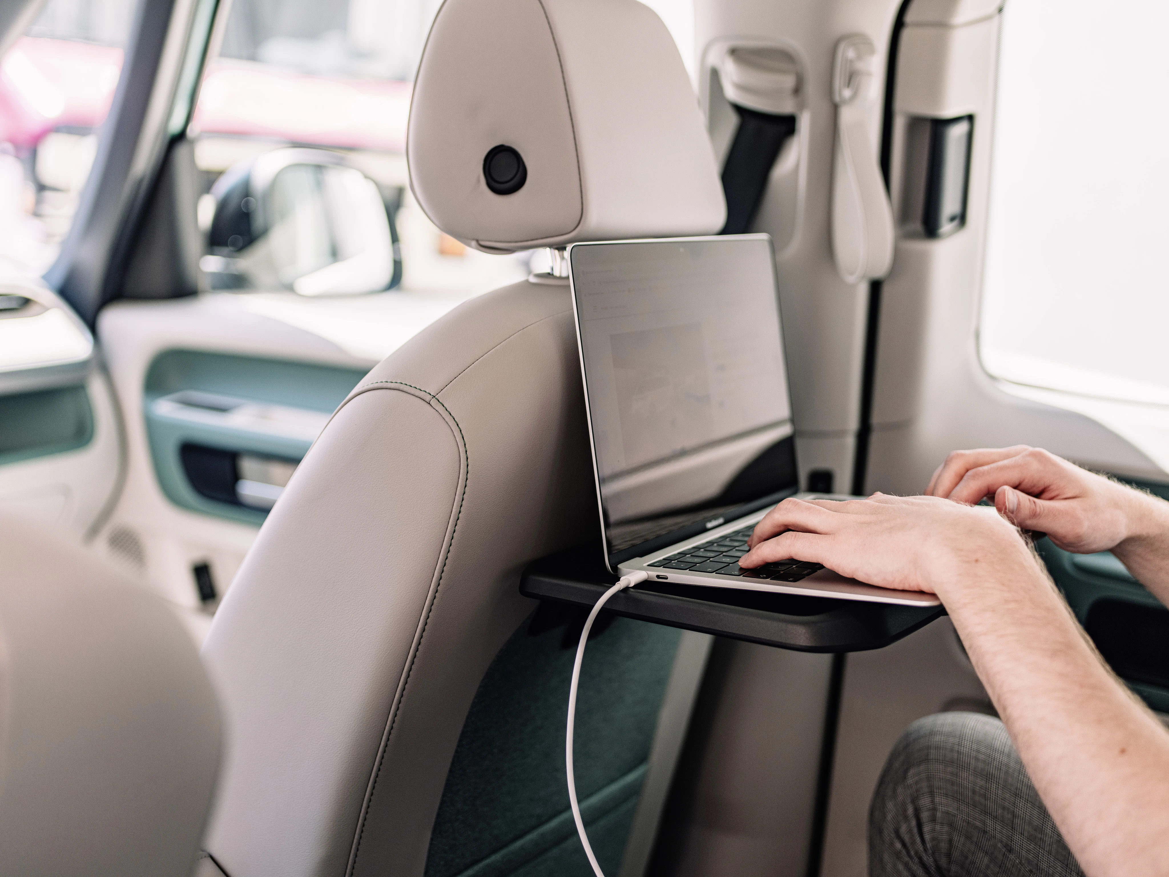 Person tippt auf einem Laptop, der auf einem Klapptisch an einer Autositzlehne steht. Das Ladekabel ist angeschlossen.