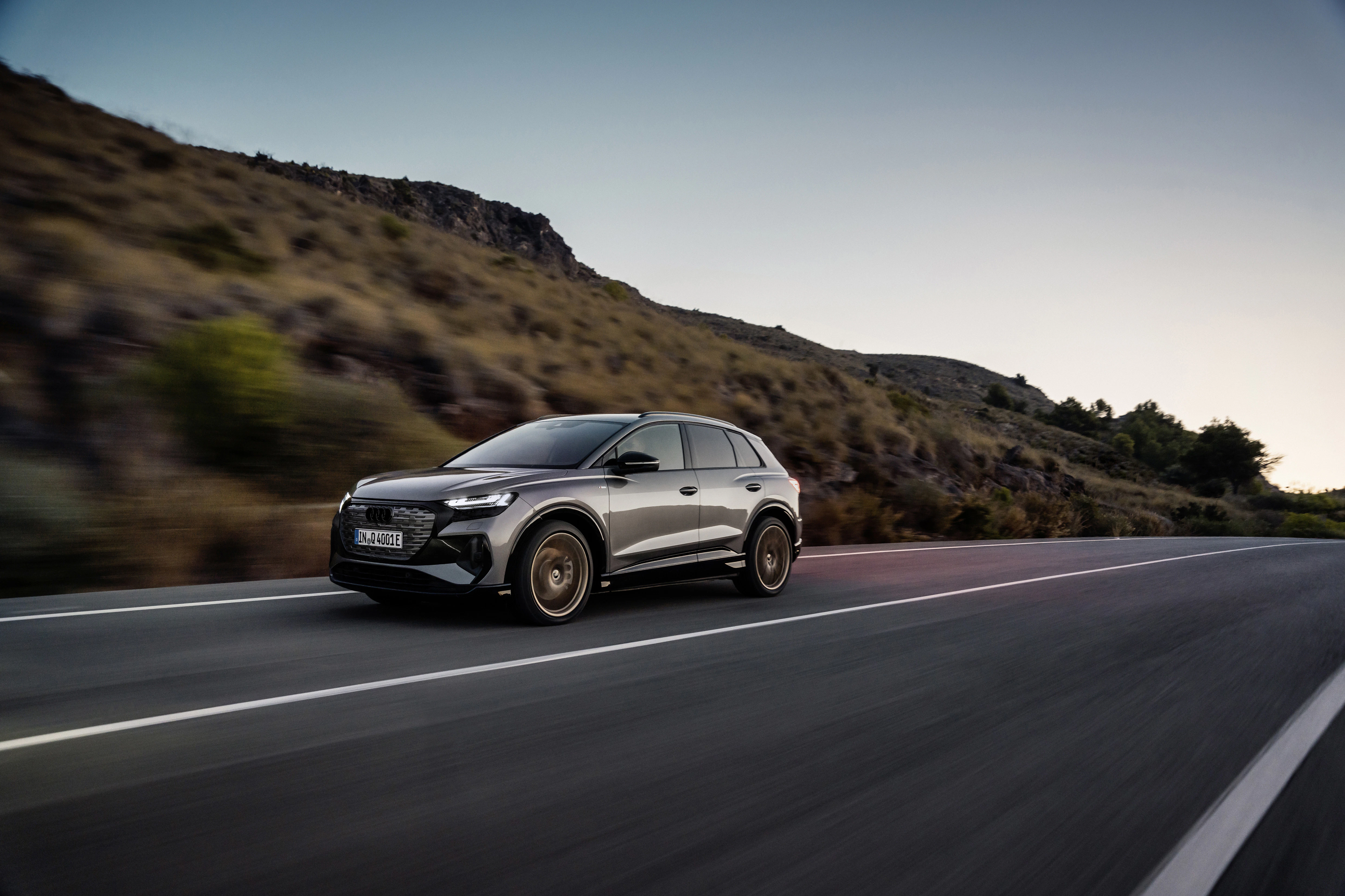 Schwarzer Elektro-SUV fährt auf einer kurvigen Landstraße durch eine hügelige Landschaft bei Sonnenuntergang.