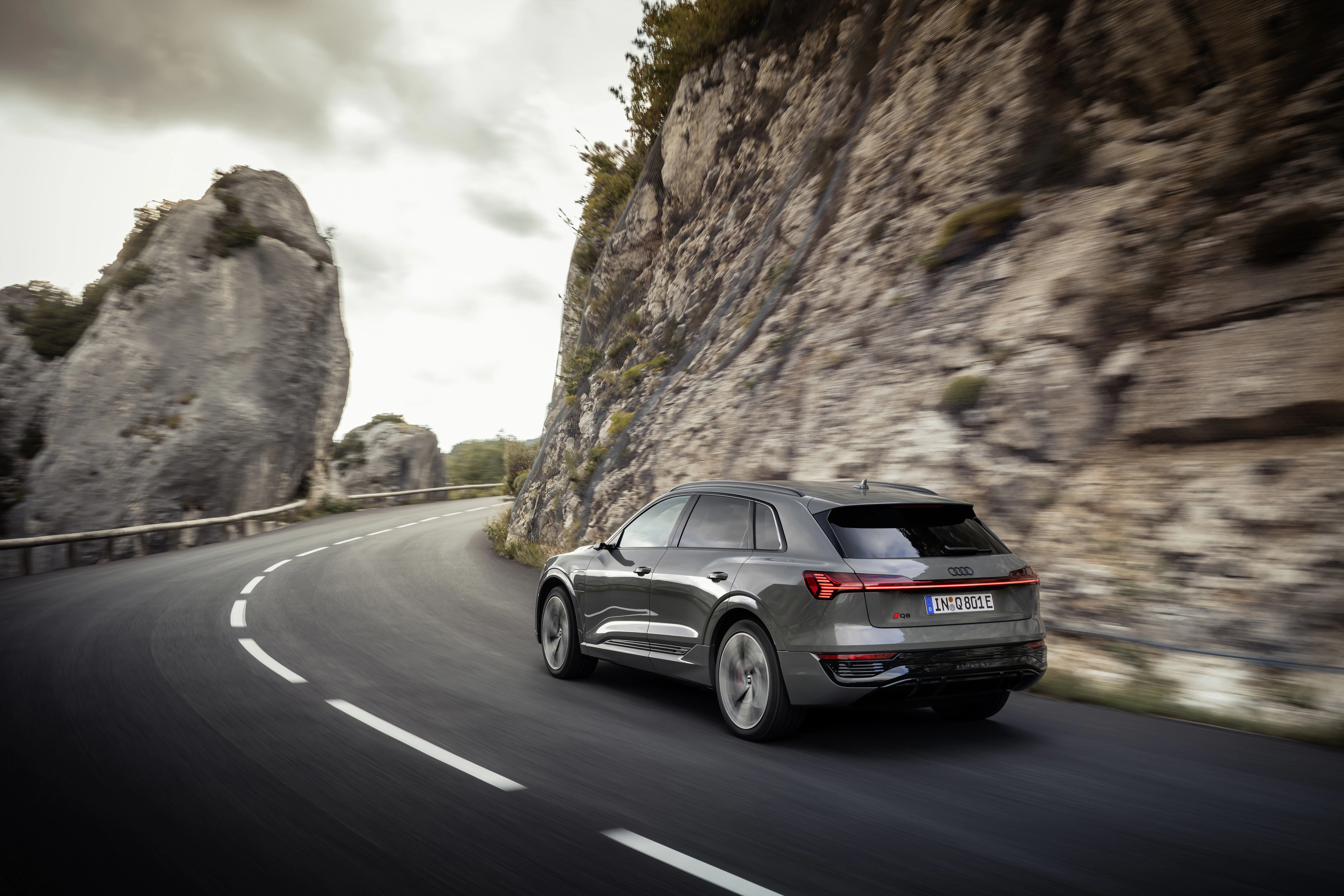 Ein grauer Audi Q8 e-tron fährt auf einer Landstraße um eine Kurve