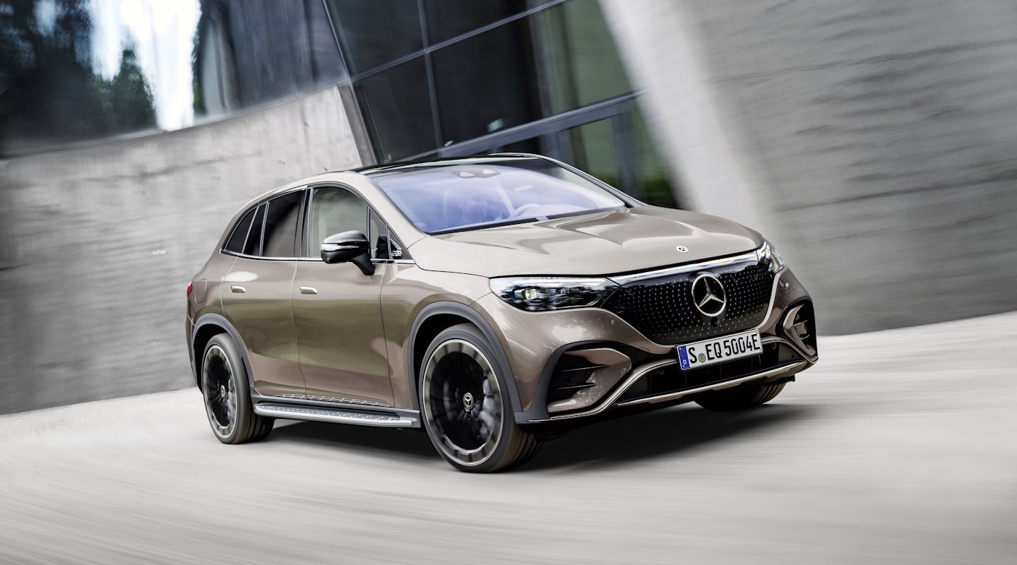 Ein bronzener Mercedes-Benz EQE SUV fährt vor einem Gebäude