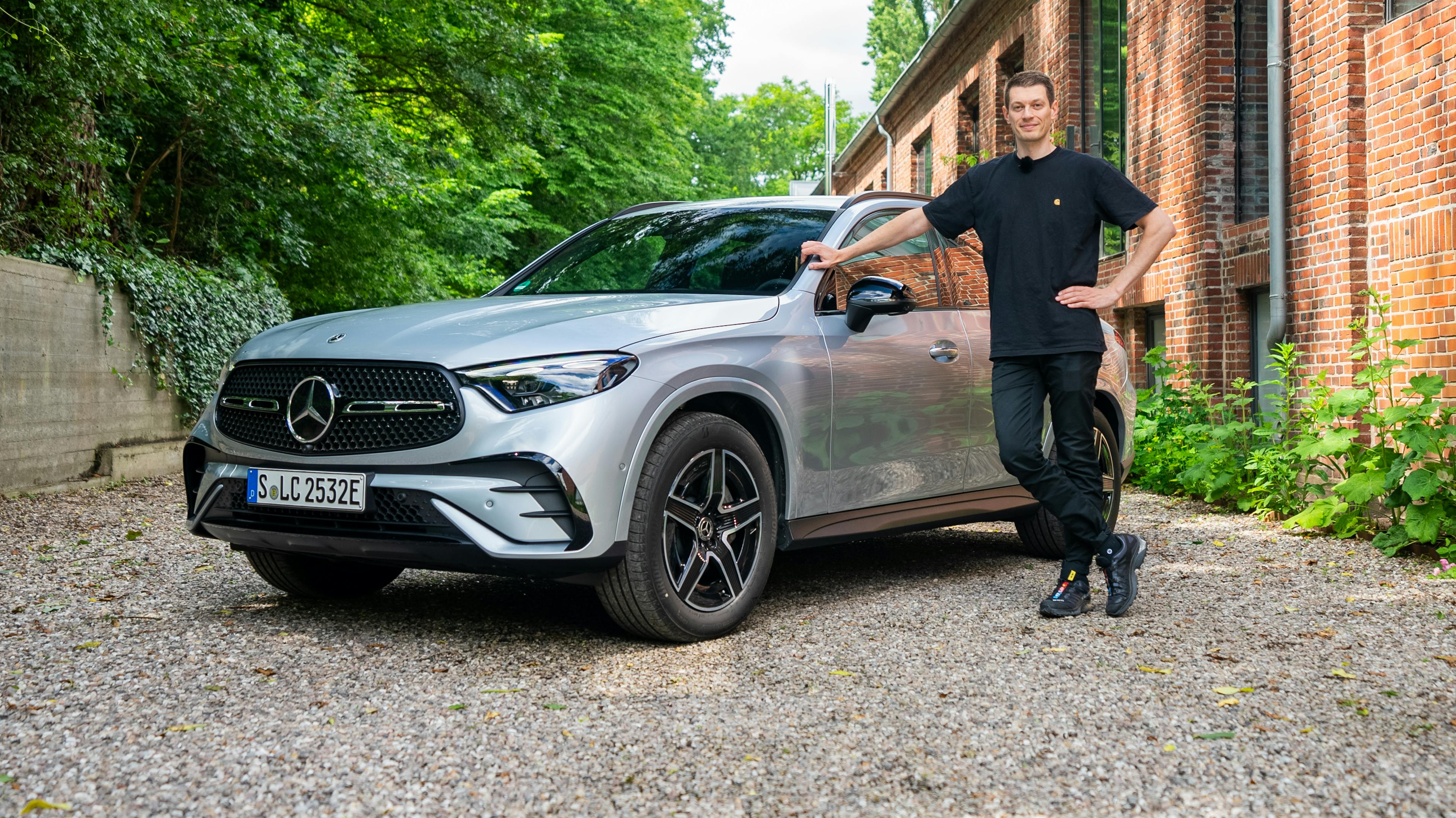  Silberner Mercedes GLC auf einem Kiesplatz mit Klinkergebäude im Hintergrund und dem Redakteur am Auto.