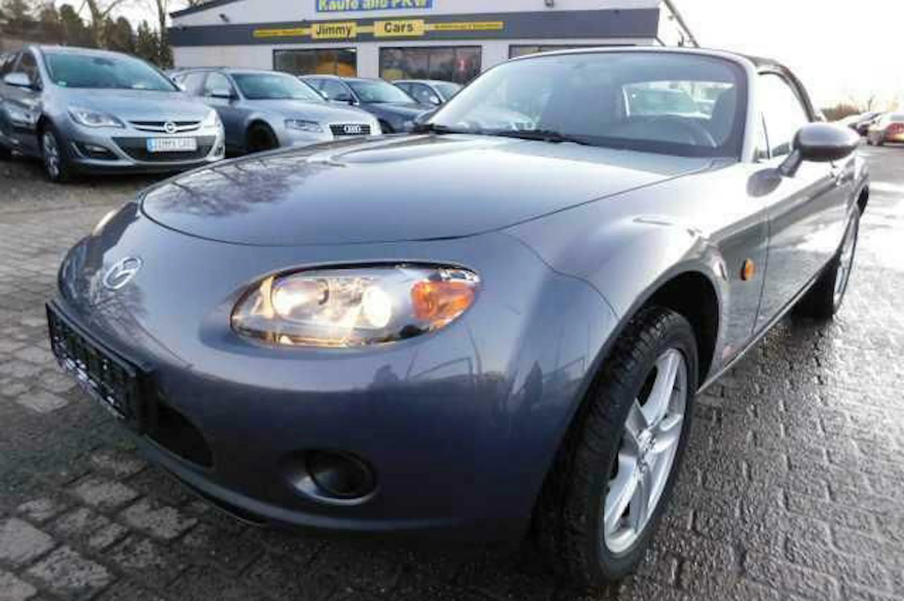 Ein grauer Mazda MX-5 parkt vor einem Autohaus.