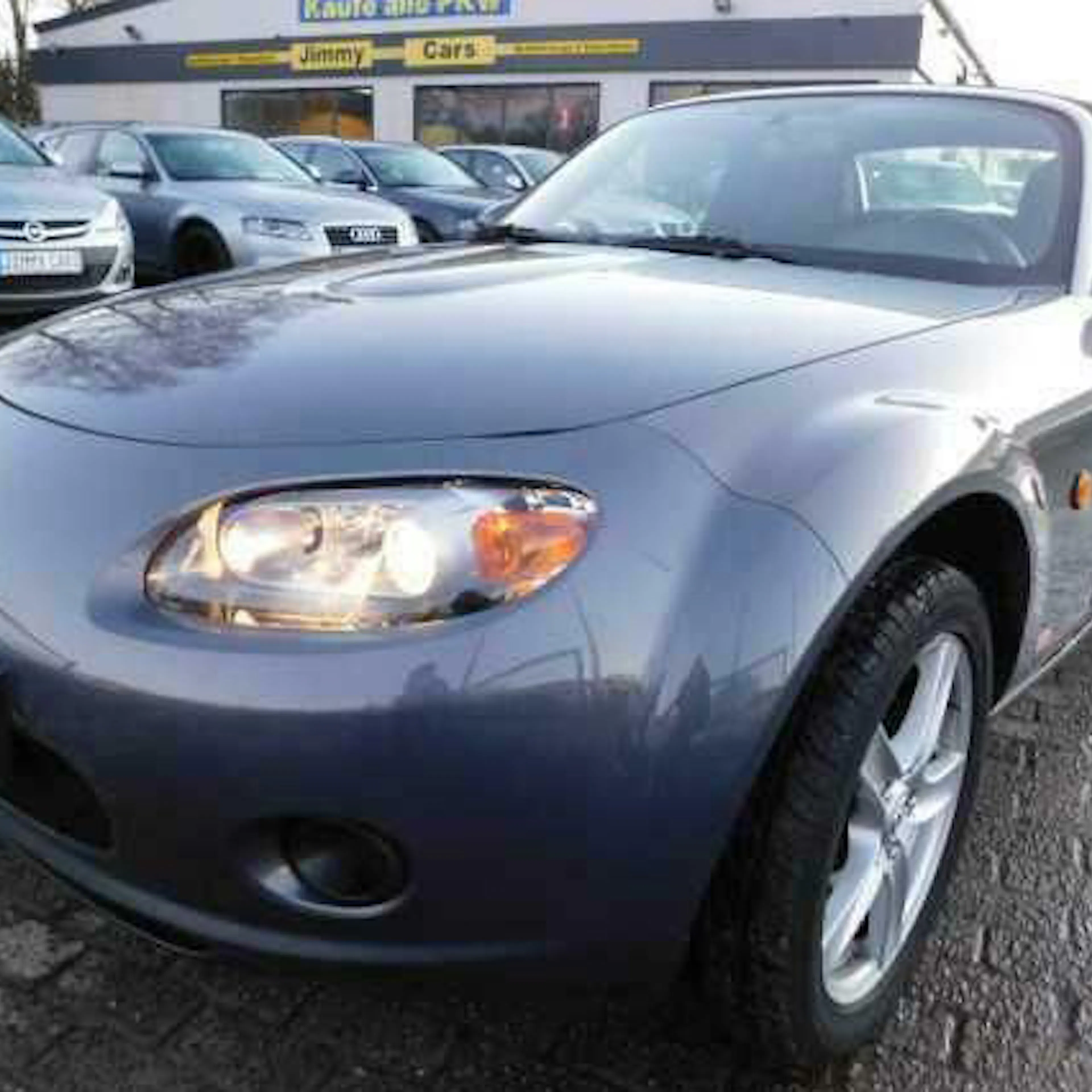 Ein grauer Mazda MX-5 parkt vor einem Autohaus.