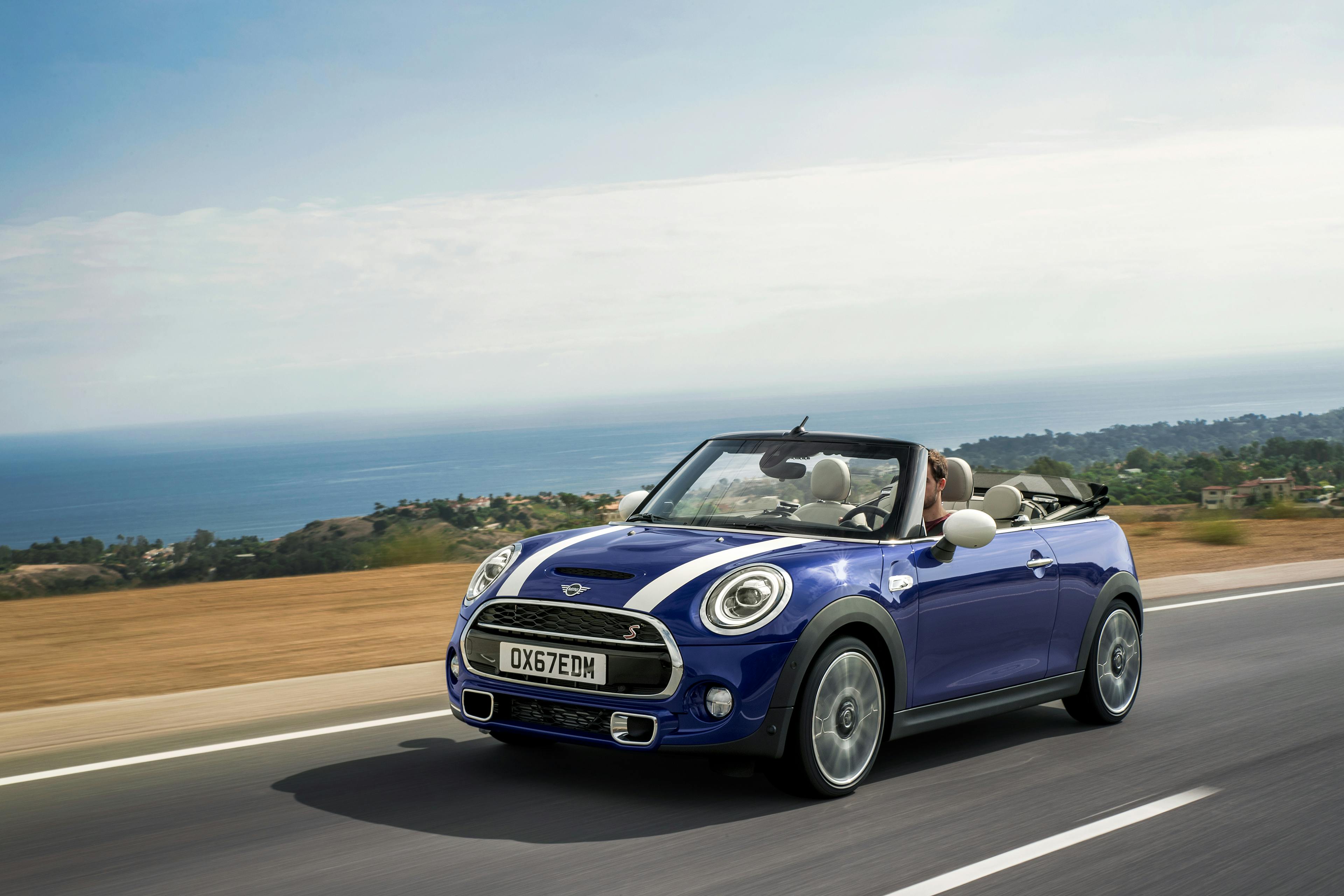 Ein blaues Mini Cabrio mit weißen Streifen auf der Motorhaube und offenem Verdeck fährt über eine Straße in den USA.