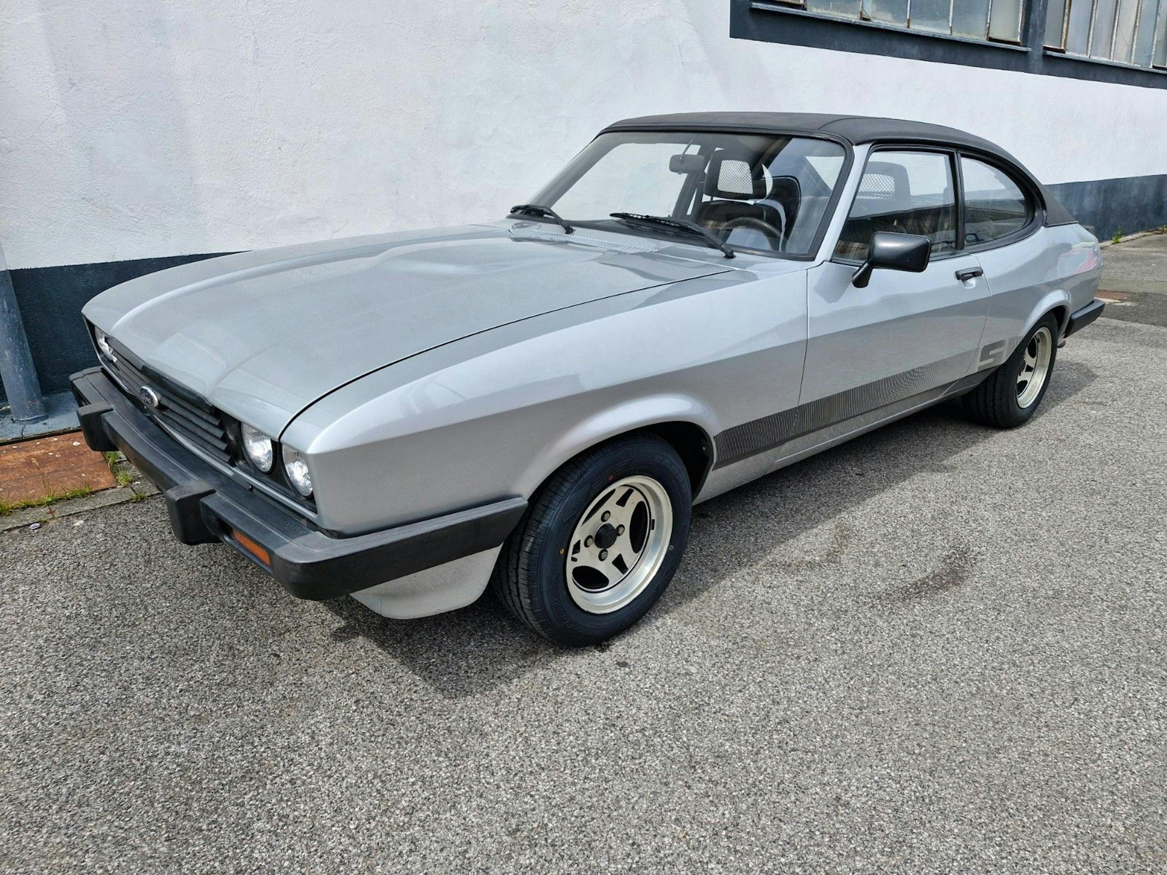 Ein silberner Ford Capri parkt vor einem weißen Gebäude.