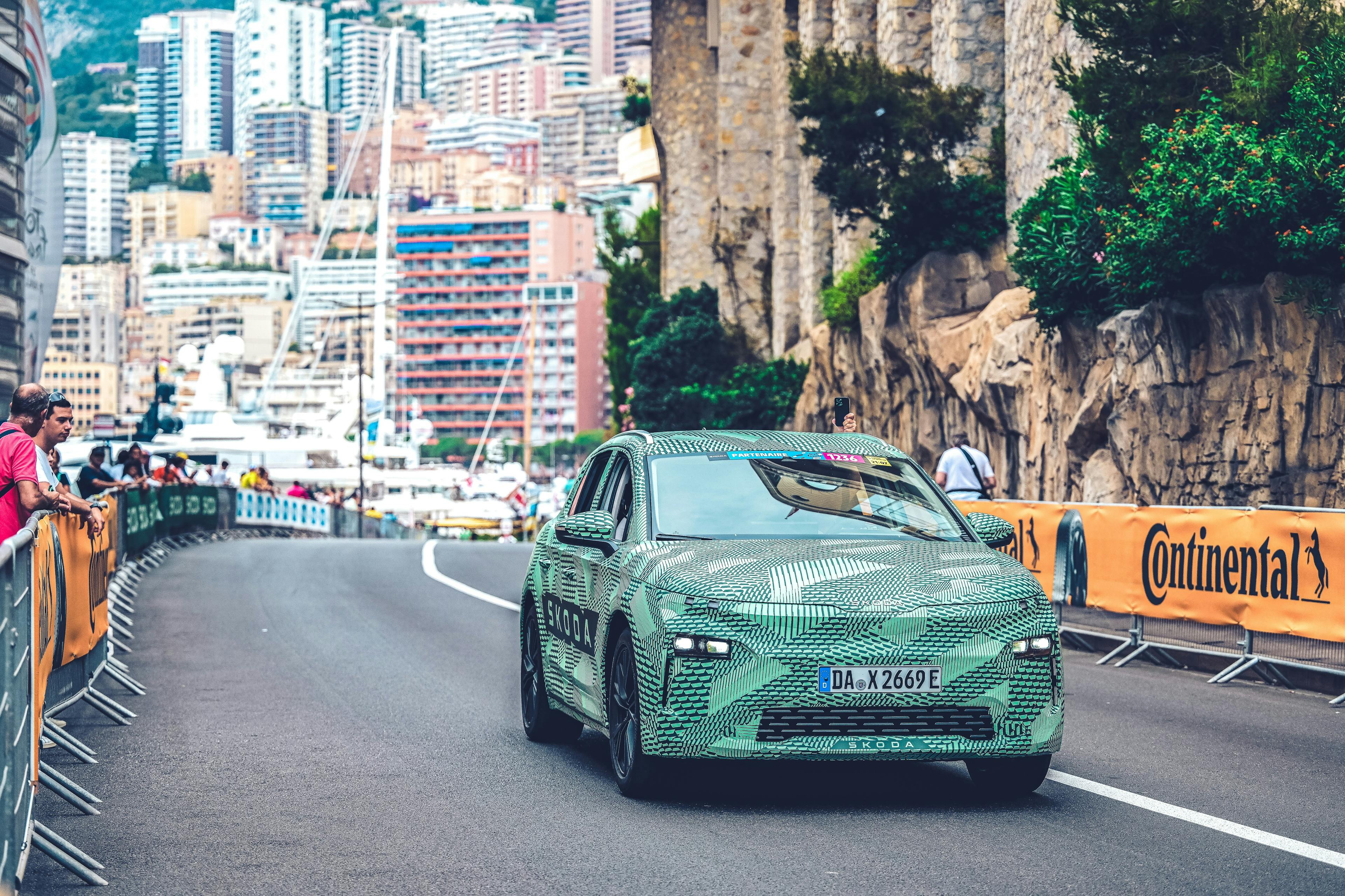 Ein mit Tarnfolie abgeklebter Škoda Elroq fährt auf der Strecke der Tour de France 2024. Im Hintergrund sind Wohngebäude von Monaco zu erkennen.