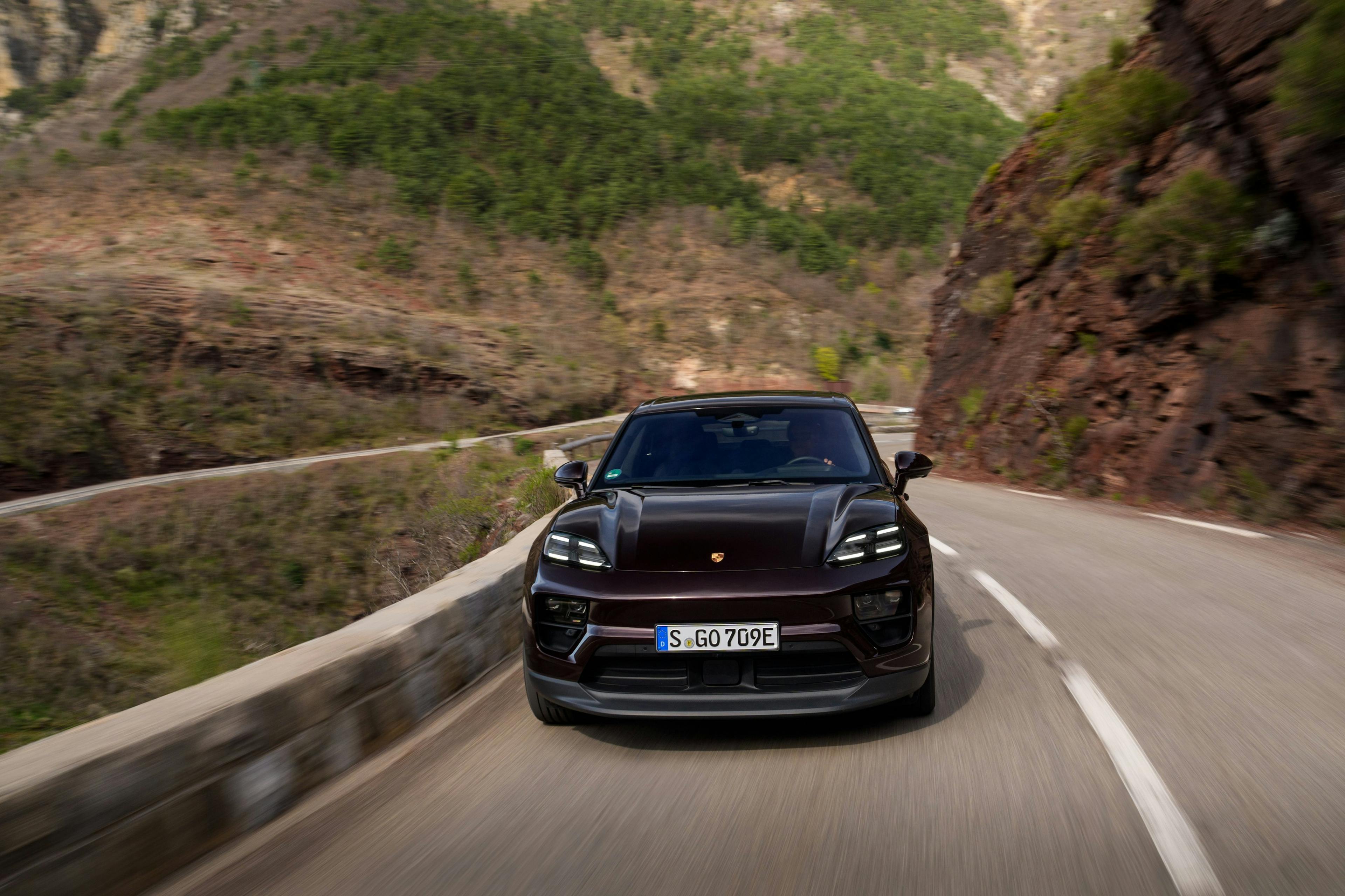 Ein schwarzer Porsche Macan Electric fährt auf einer Bergstraße auf den Betrachter des Bildes zu.