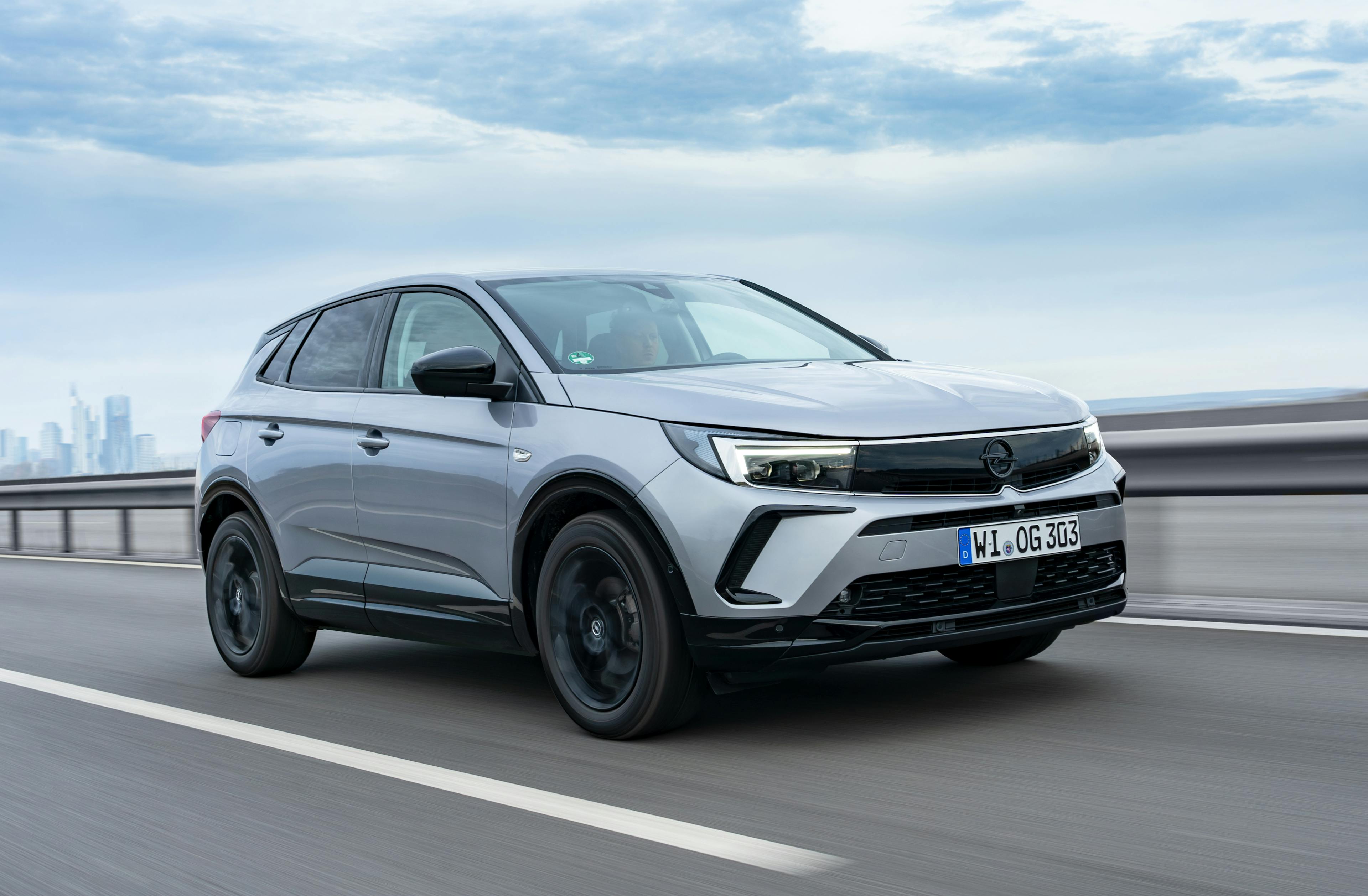 Ein metallic-grauer Opel Grandland fährt auf einer Schnellstraße von links nach rechts durch das Bild.