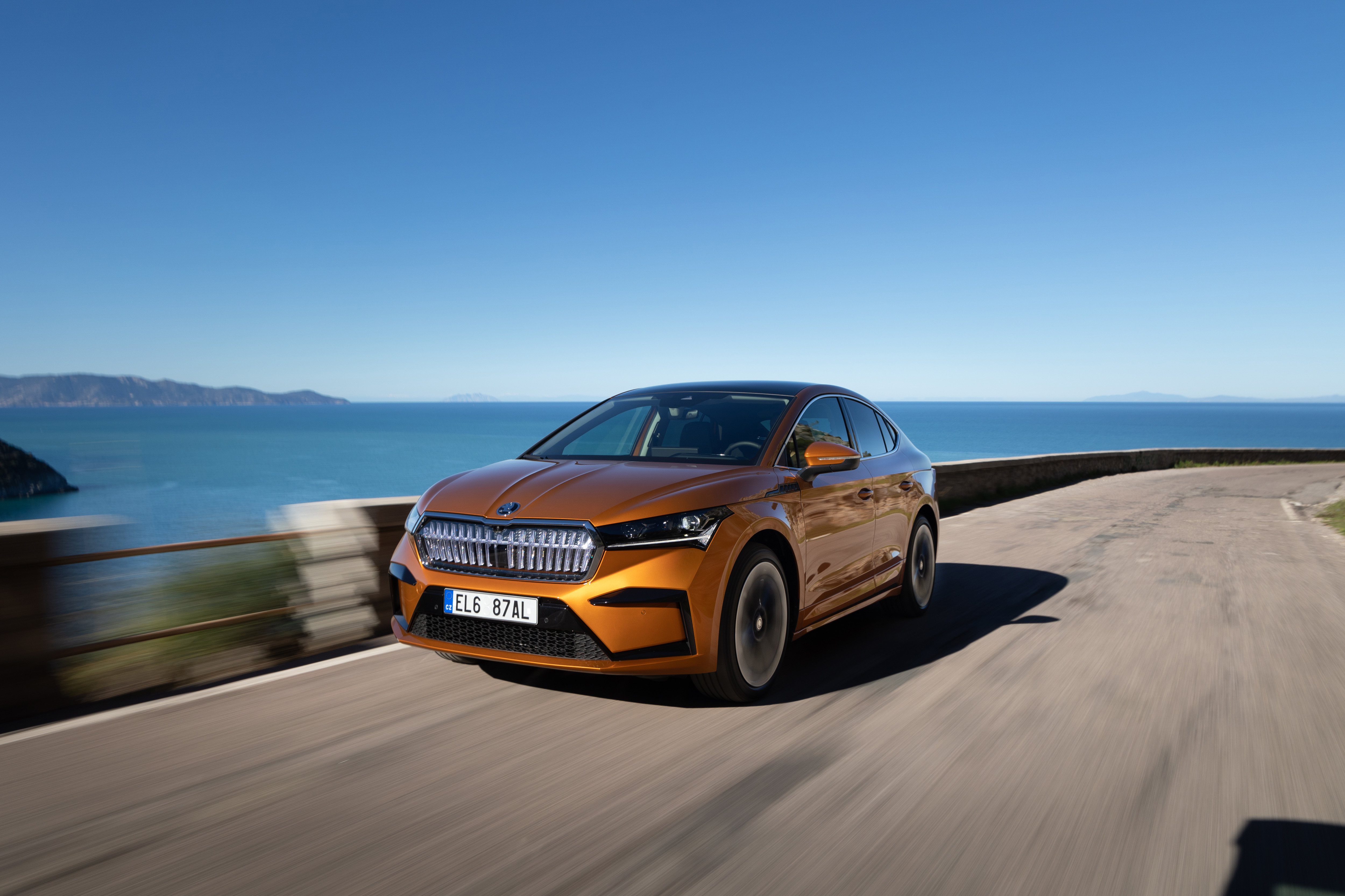 Ein oranger Škoda Enyaq fährt auf einer Küstenstraße