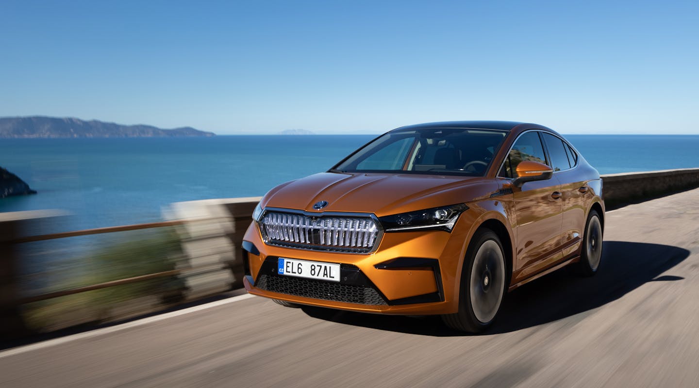 Ein oranger Škoda Enyaq fährt auf einer Küstenstraße
