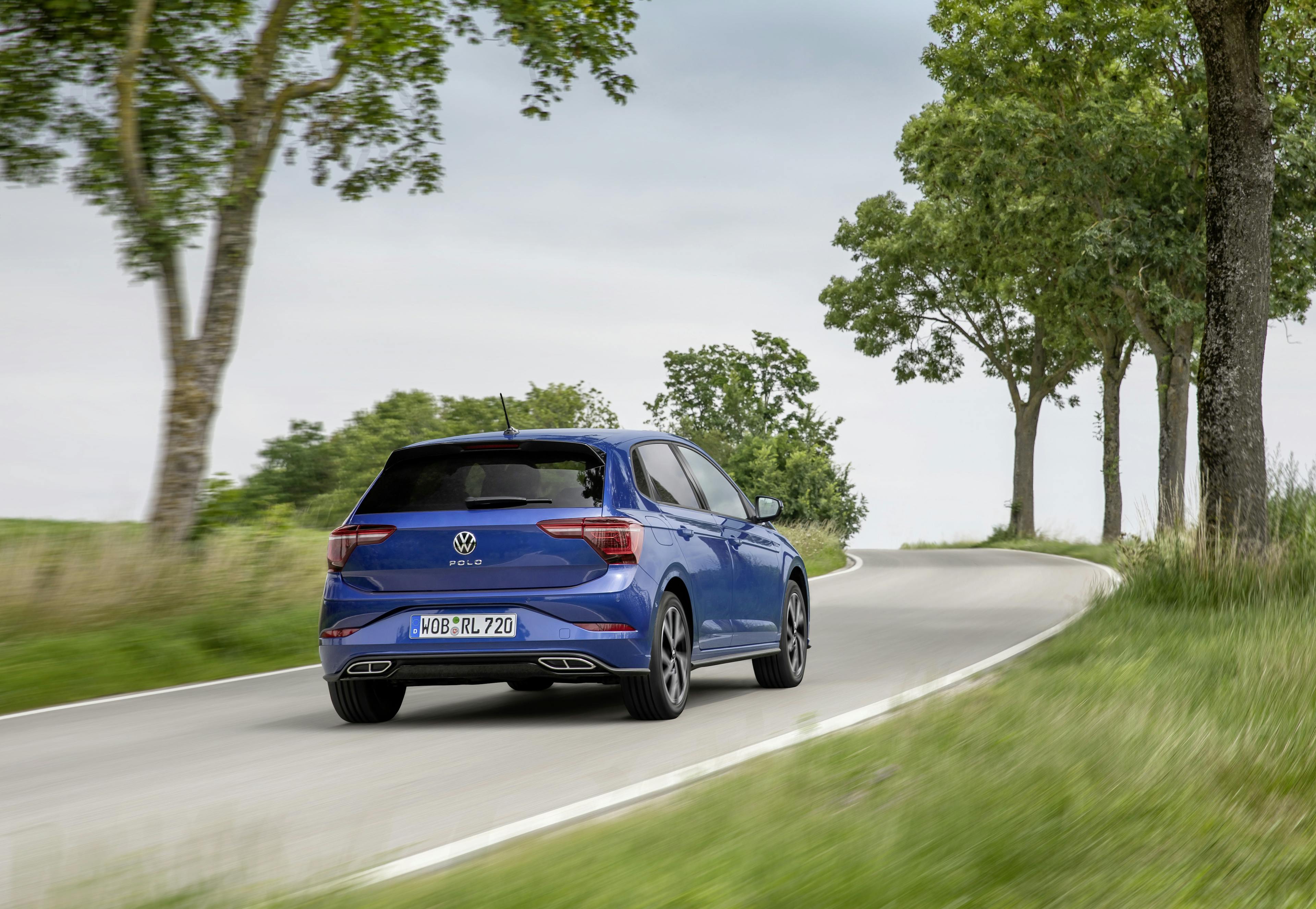 Ein blauer VW Polo 6 fährt auf einer kurvigen Straße mit Bäumen und grüner Landschaft.