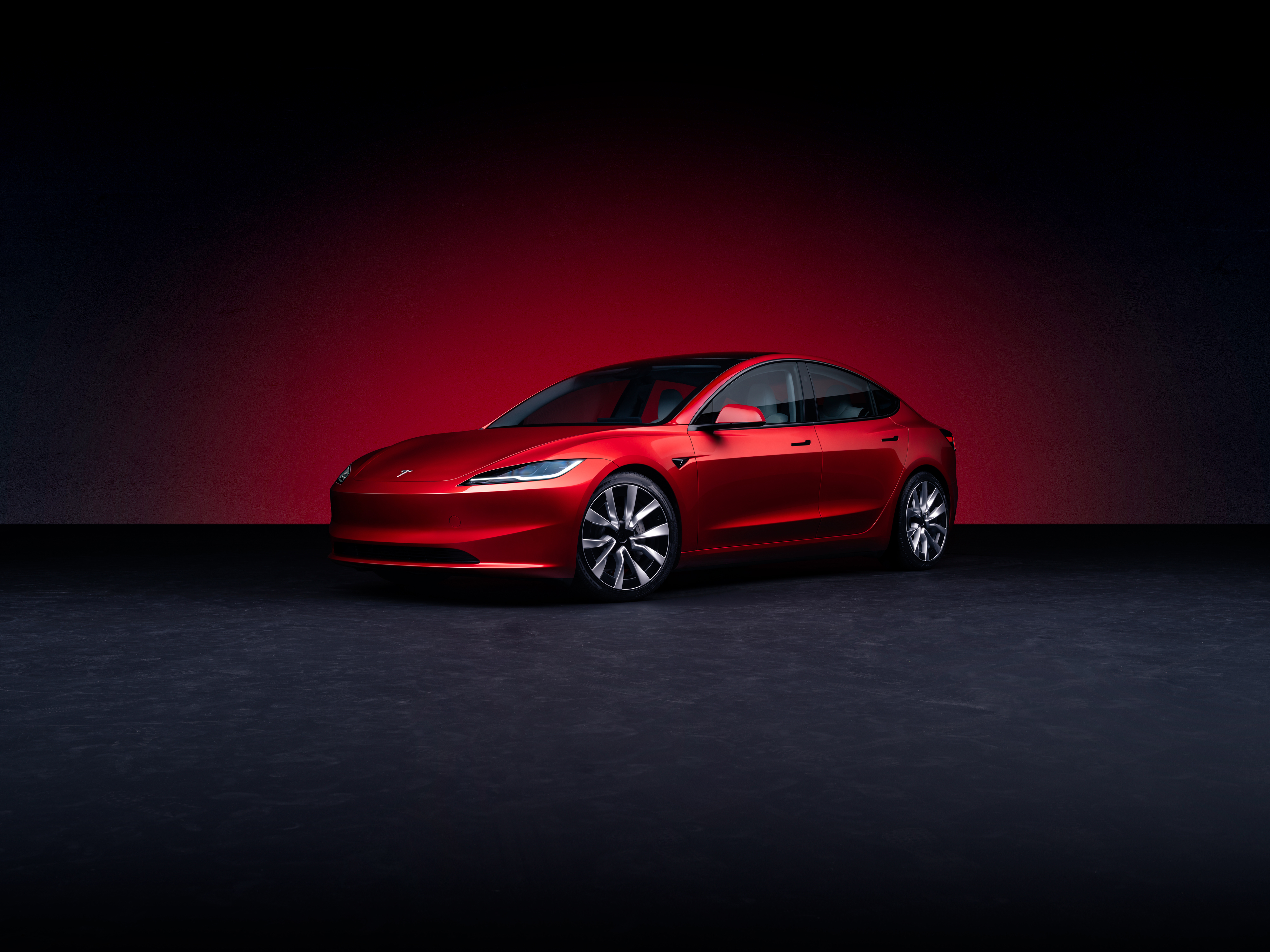 ein roter Tesla Model 3 steht vor einem dunklen Hintergrund