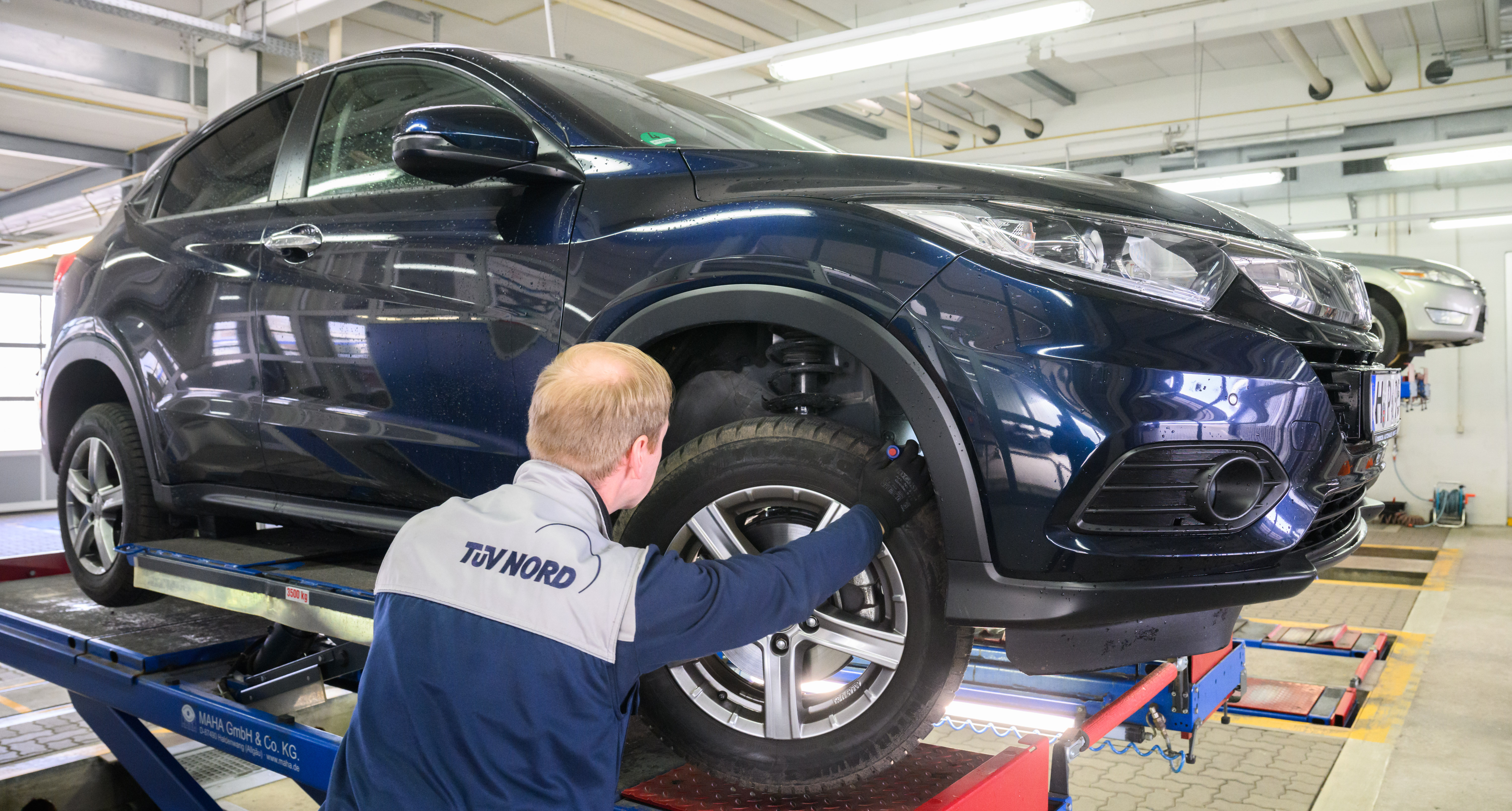 Ein TÜV-Prüfer untersucht ein Auto, das auf einer Hebebühne steht.