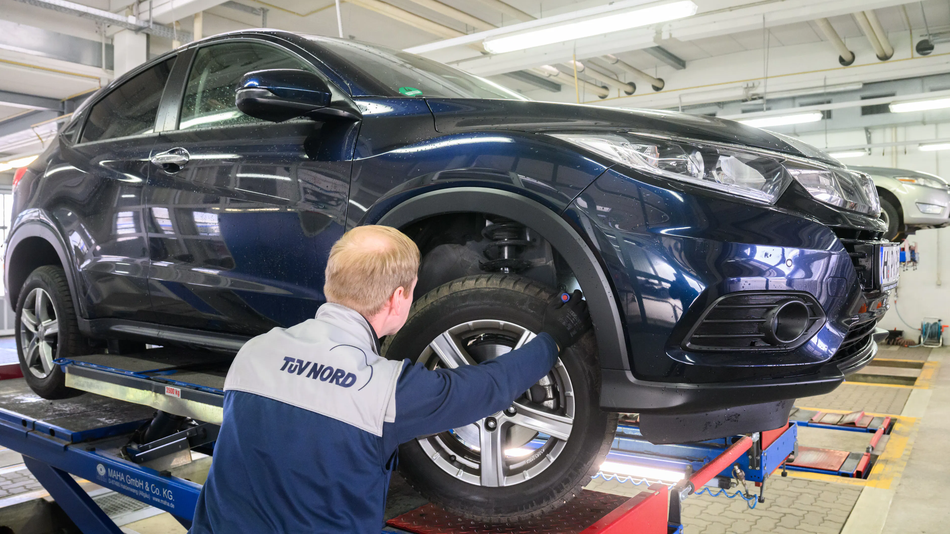 Ein TÜV-Prüfer untersucht ein Auto, das auf einer Hebebühne steht.