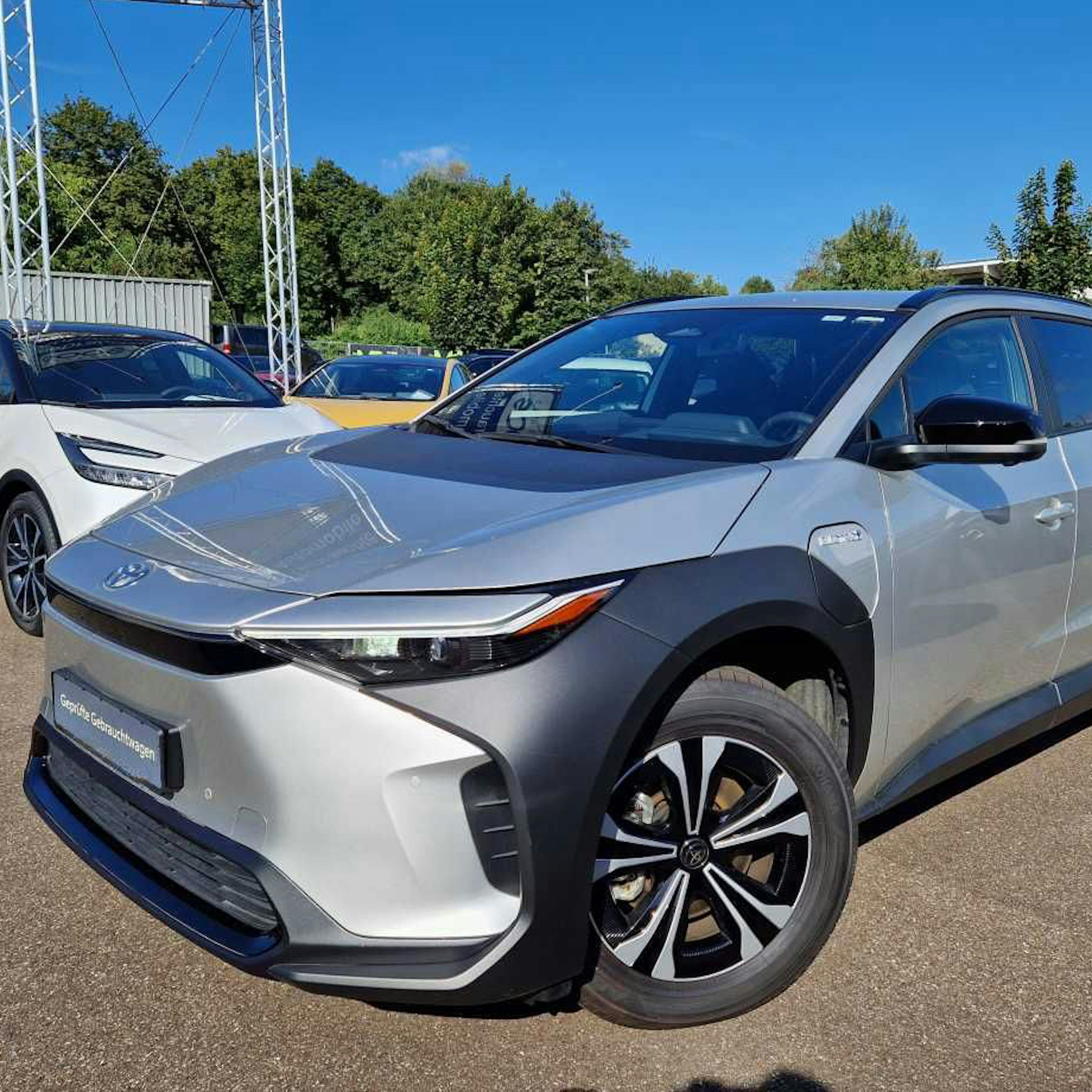 A silver Toyota bZ4X in the yard of a car dealer.